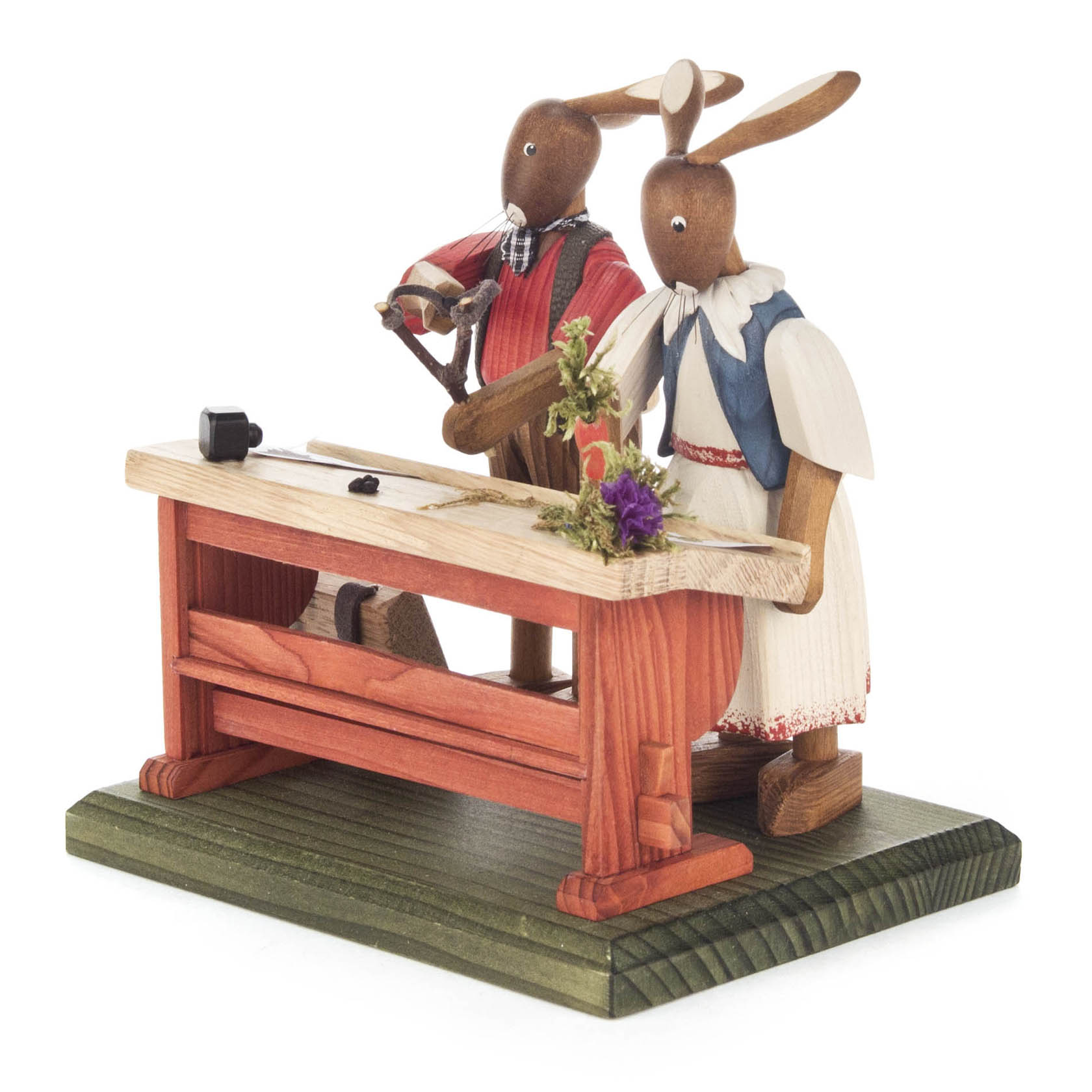 Zwei Hasenfiguren, eine männlich und eine weiblich, stehen an einem Holztisch mit einer Säge und Pflanzen. Beide tragen traditionelle Kleidung. im Dregeno Online Shop günstig kaufen
