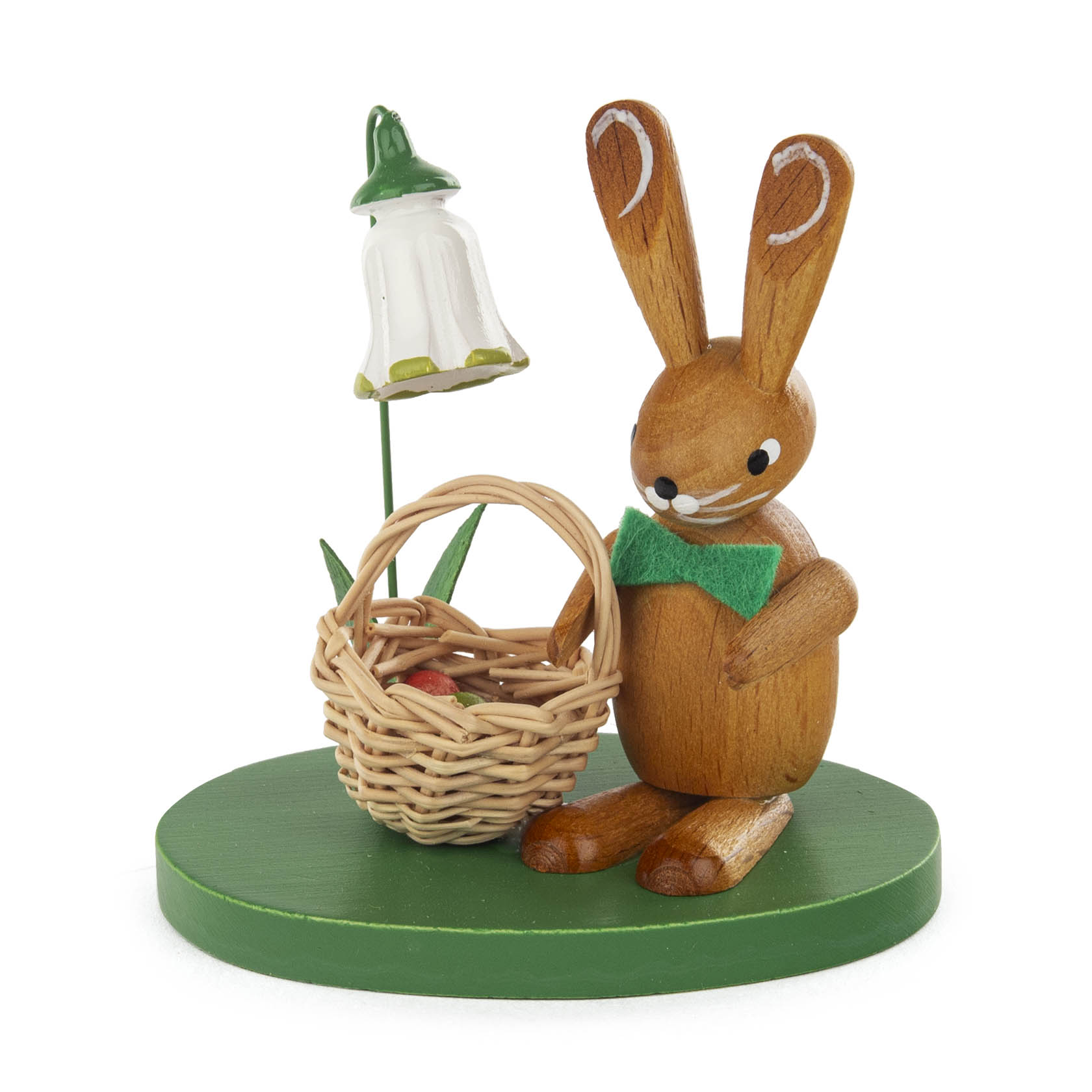 Holzhase mit grüner Fliege, einen Korb mit rotem Ei haltend, neben einer weißen Blume mit gelbem Rand auf einem grünen Sockel. im Dregeno Online Shop günstig kaufen