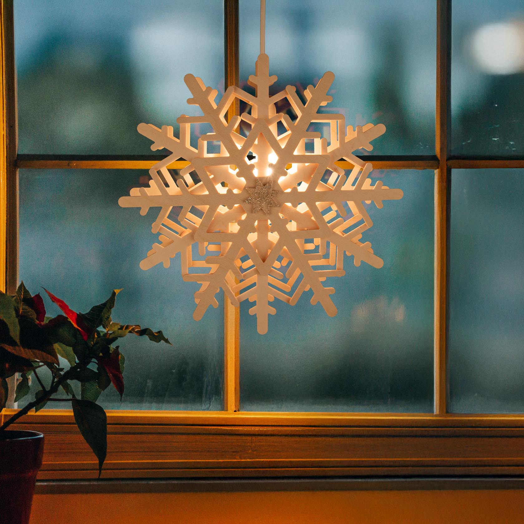 Ein beleuchteter Schneekristall als Fensterdekoration, der an einem Fenster hängt. Die Schneeflocke hat ein detailliertes geometrisches Design.