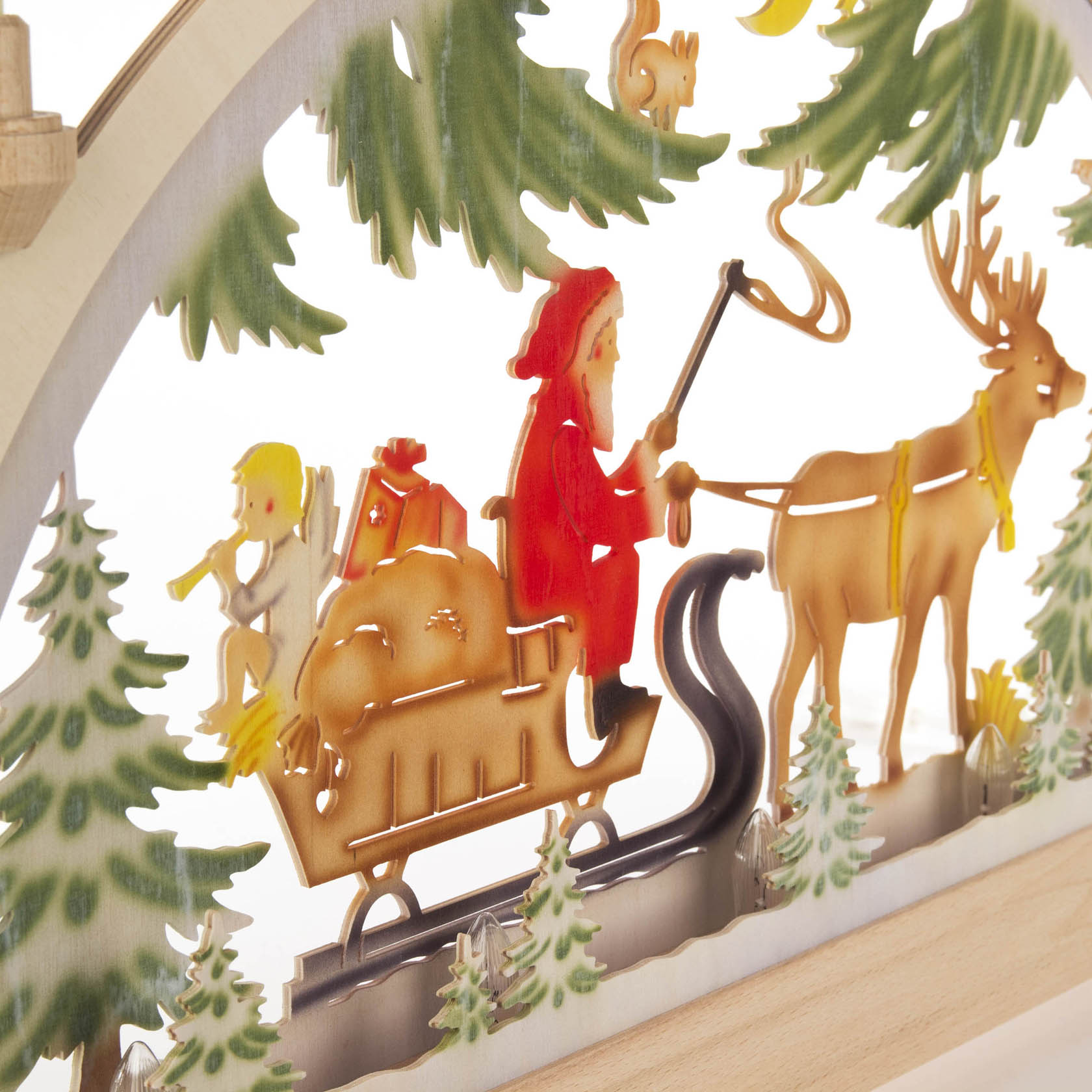 Ein bunter Schwibbogen zeigt Nikolaus in rotem Mantel auf einem Schlitten voller Geschenke, gezogen von einem Rentier im verschneiten Wald. Er ist elektrisch beleuchtet.