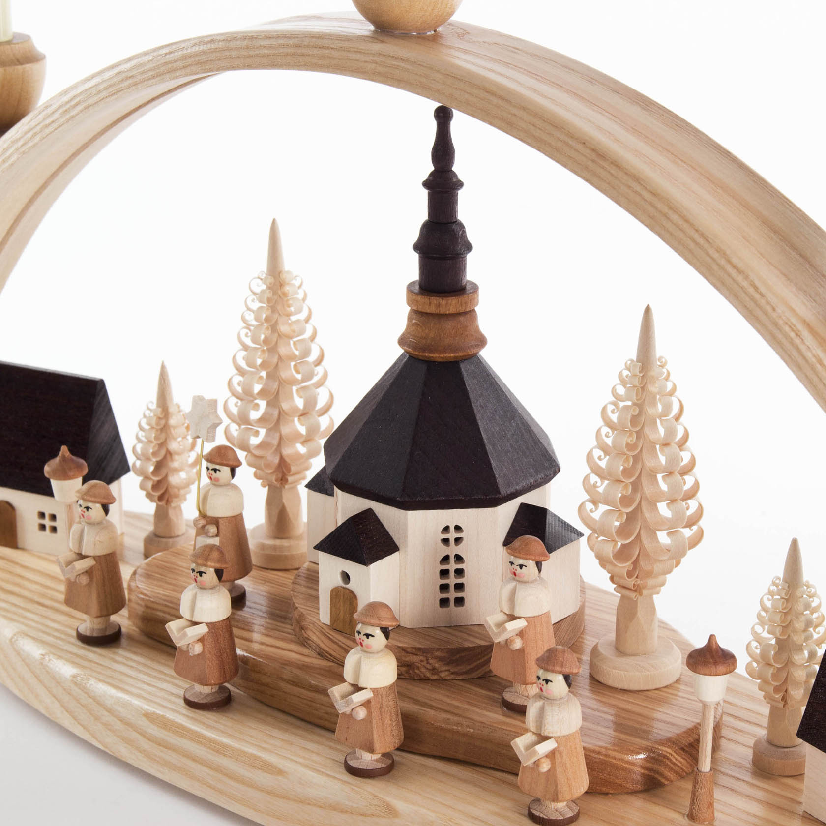Ein Schwibbogen zeigt ein Miniaturdorf mit einer Kirche in der Mitte, umgeben von Kurrendefiguren und Tannen aus Holz, elektrisch beleuchtet.