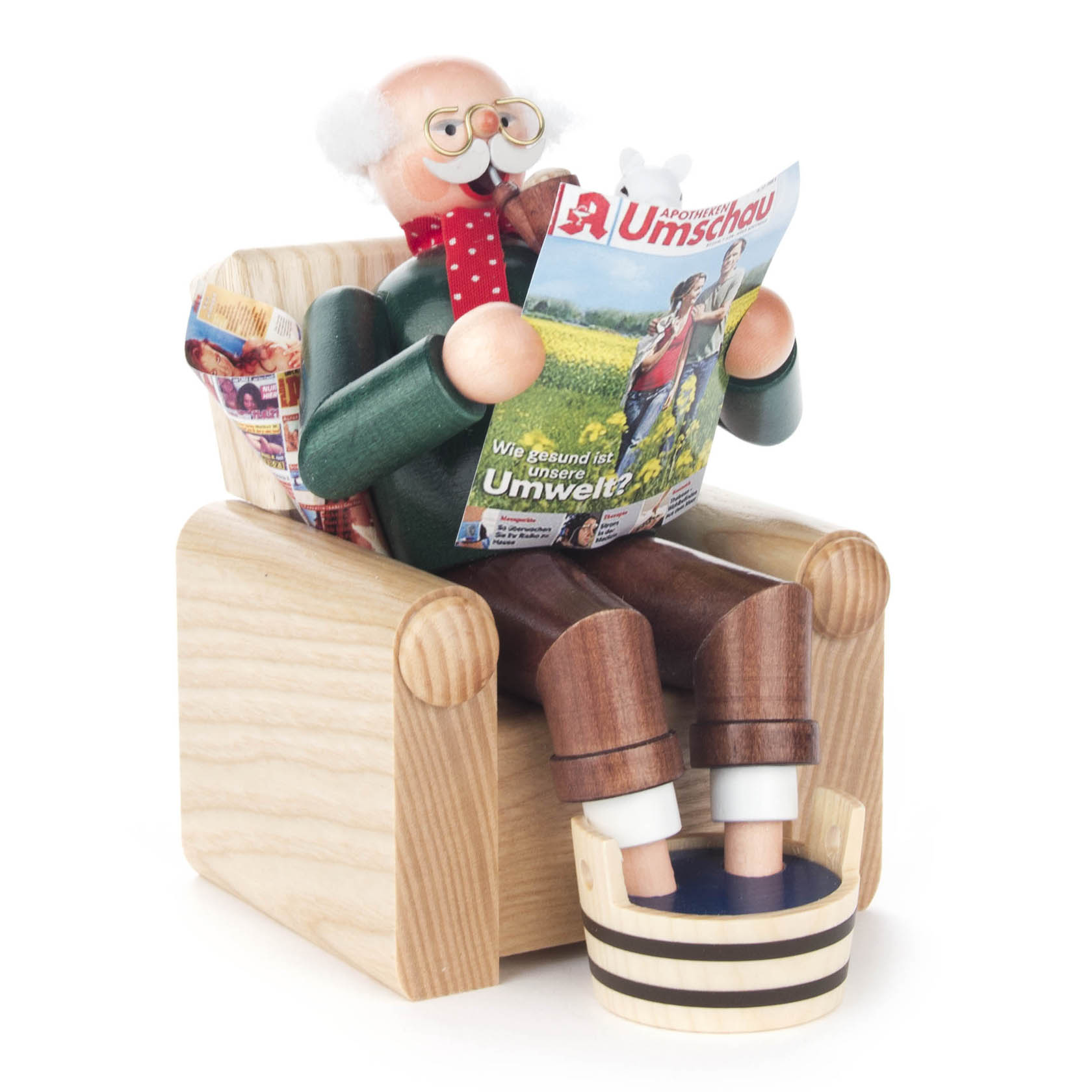 Ein traditioneller Räuchermann in Form eines sitzenden Opas in einem Holzsessel, der eine Zeitung liest. Vor ihm ein Fußbad und er trägt eine Brille sowie eine rote Fliege.