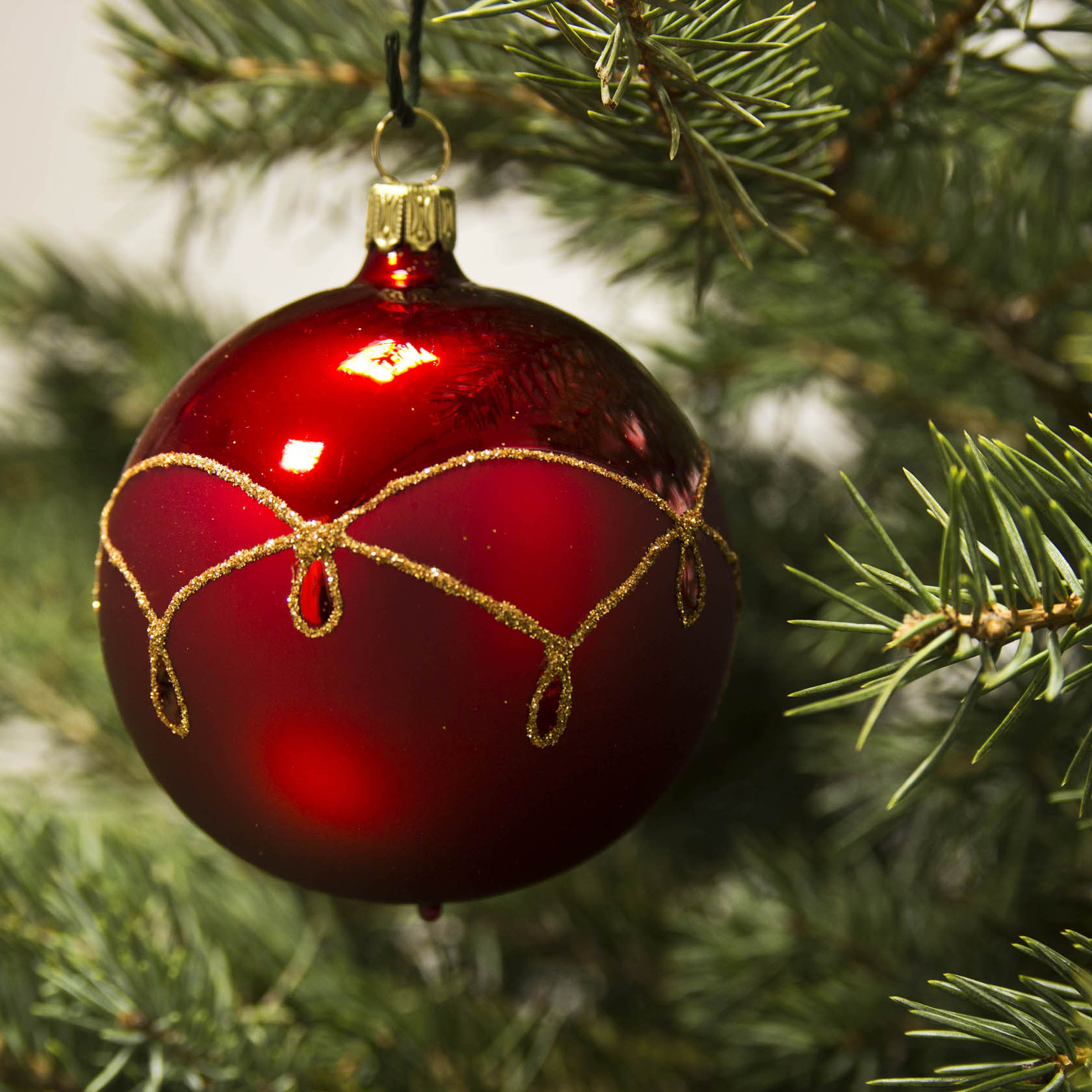 A red matte Christmas ornament ball with a gold drop pattern, hanging on a green Christmas tree branch.