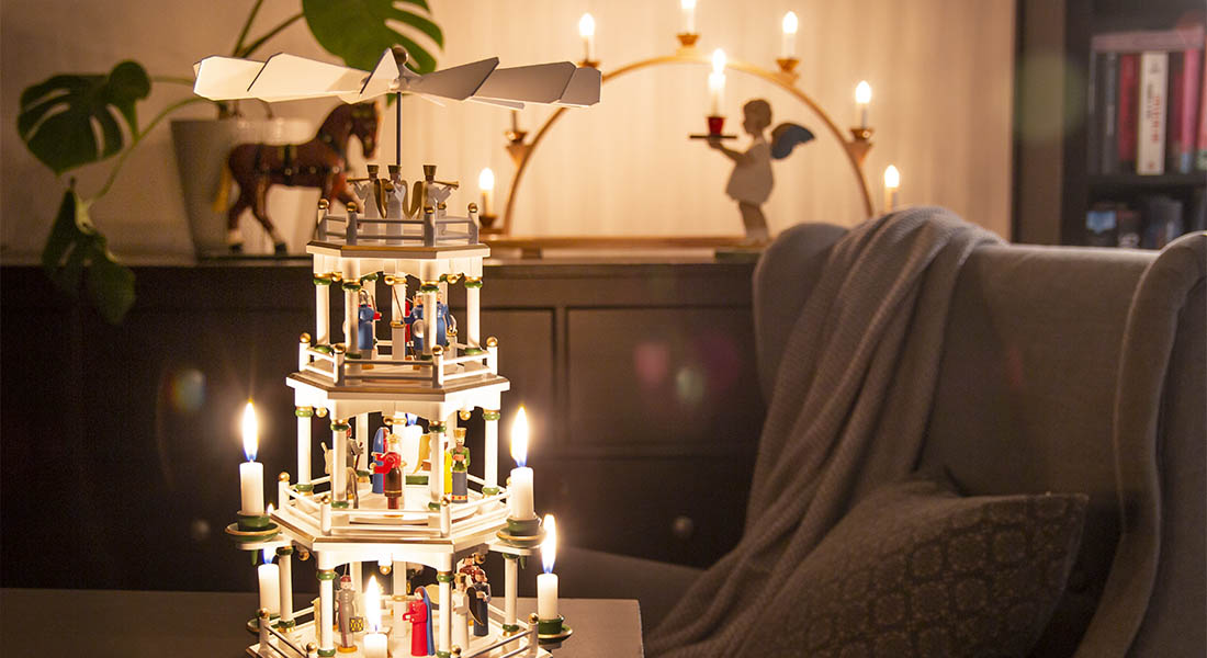 Eine mehrstöckige erzgebirgische Weihnachtspyramide mit brennenden Kerzen steht in einem Wohnzimmer