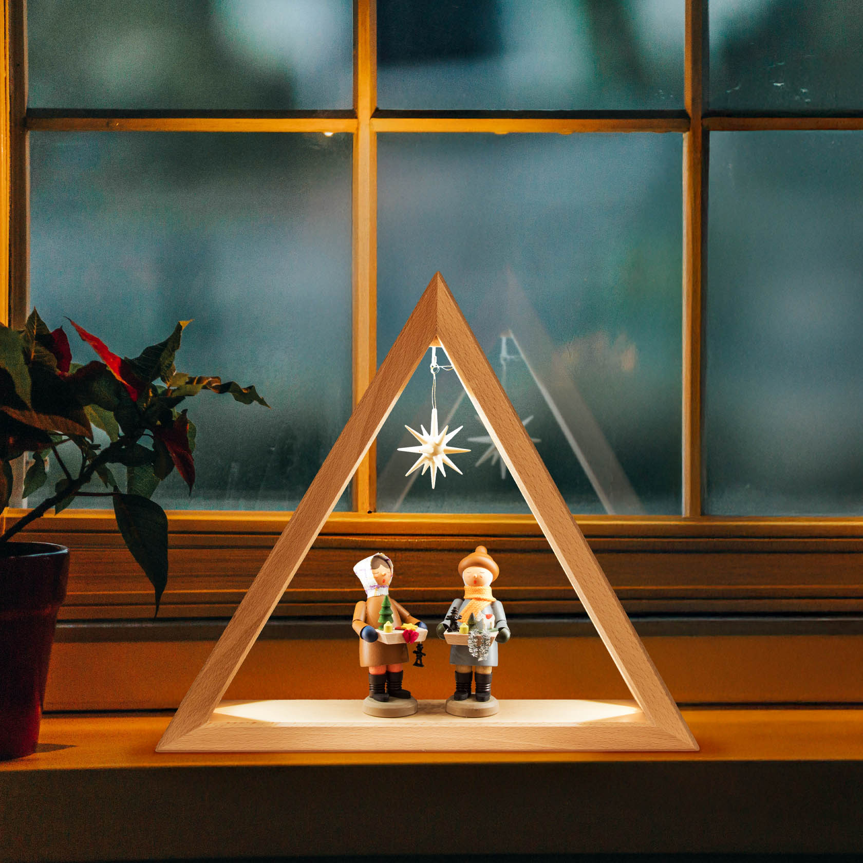 Ein beleuchtetes Dreieck aus Holz, das mit LED-Band hinterleuchtet ist. Im Inneren stehen zwei traditionelle Figuren und ein leuchtender Stern.