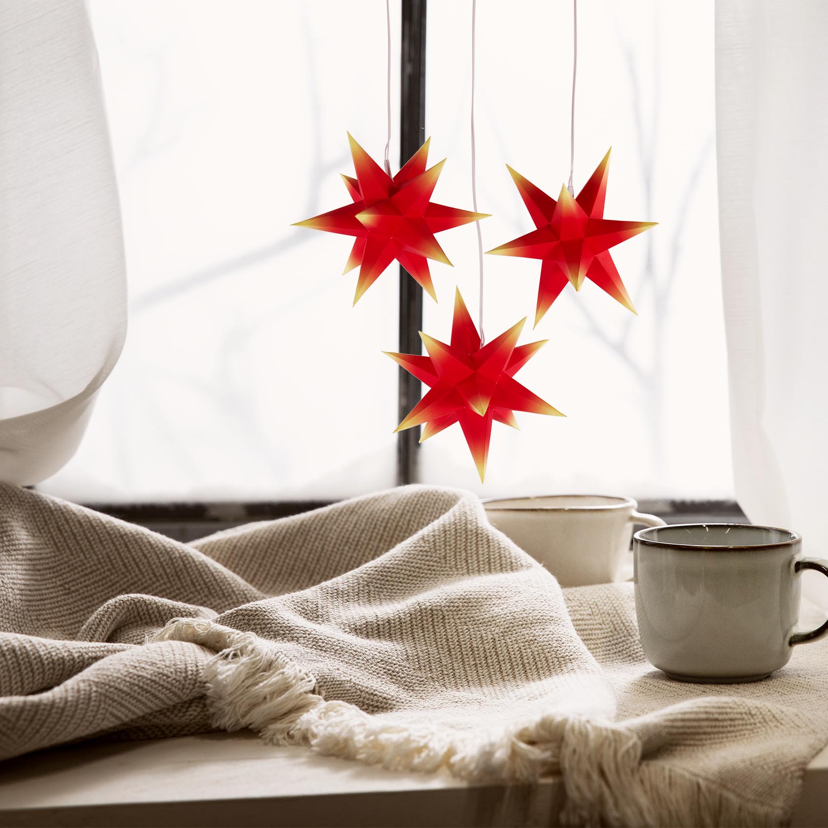 Drei Mini-Adventssterne mit roten Körpern und gelben Spitzen hängen nebeneinander, alle mit elektrischer Beleuchtung ausgestattet.