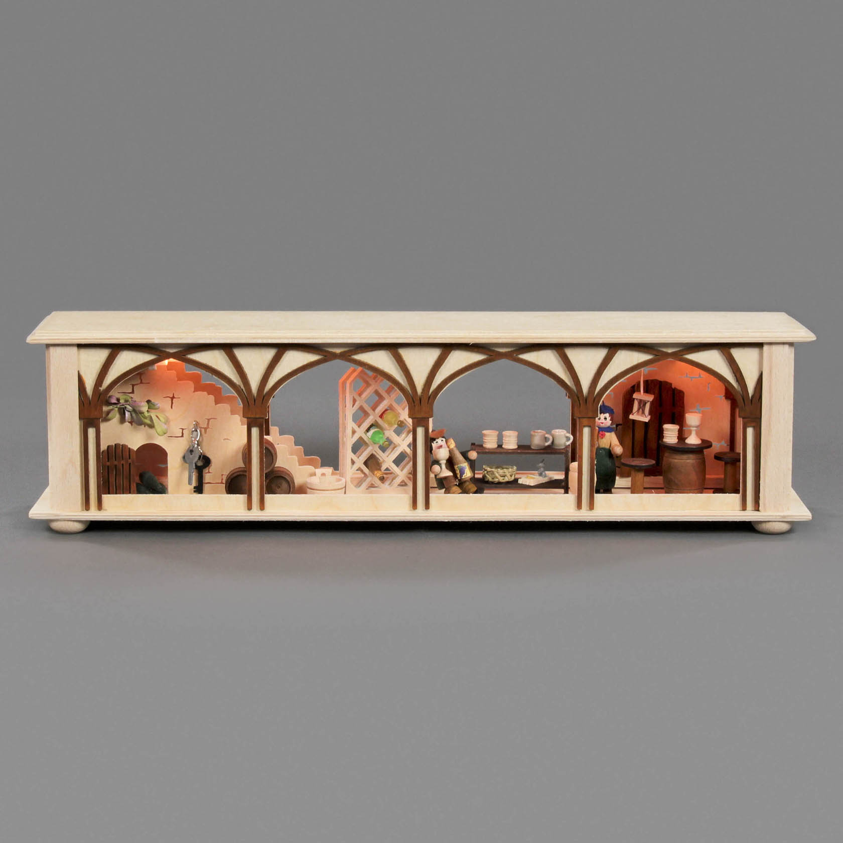 Holzminiatur eines Weinkellers mit drei beleuchteten Kammern. Links ein Türbogen und Treppe, Mitte ein Tisch mit Flaschen, rechts Regale mit Fässern.