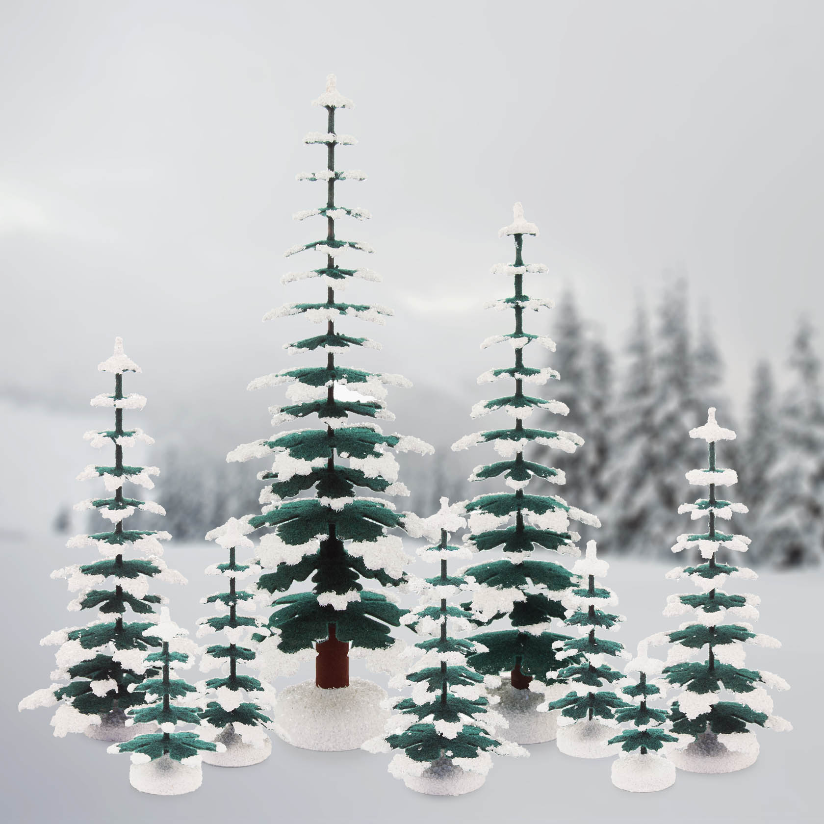 Mehrere kleine, schneebedeckte Modell-Fichtentannen in verschiedenen Größen stehen auf einer weißen Fläche.