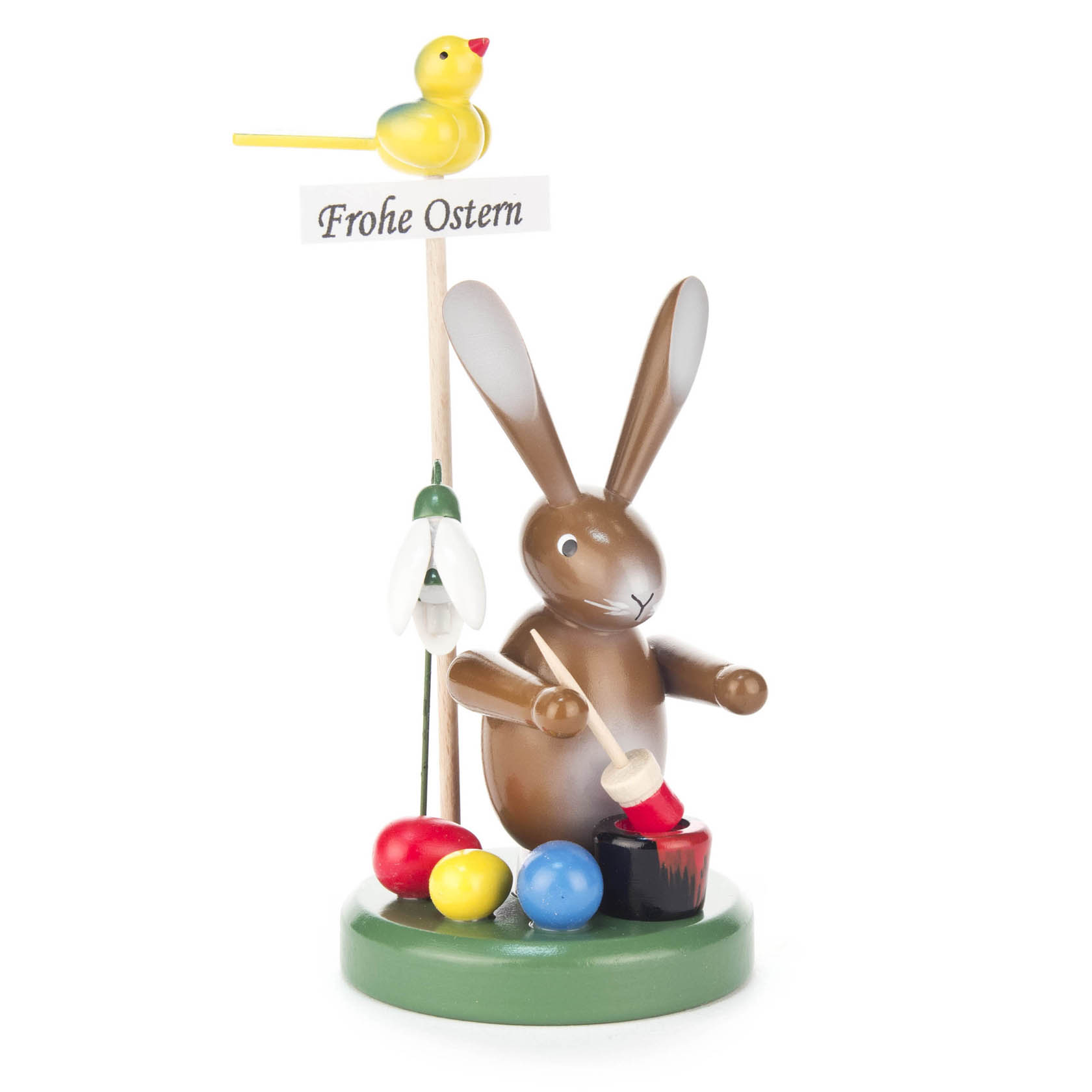 Eine Hasenfigur mit braunem Fell bemalt Ostereier. Daneben eine Blume und ein Schild mit 'Frohe Ostern'. Oben sitzt ein gelber Vogel. im Dregeno Online Shop günstig kaufen