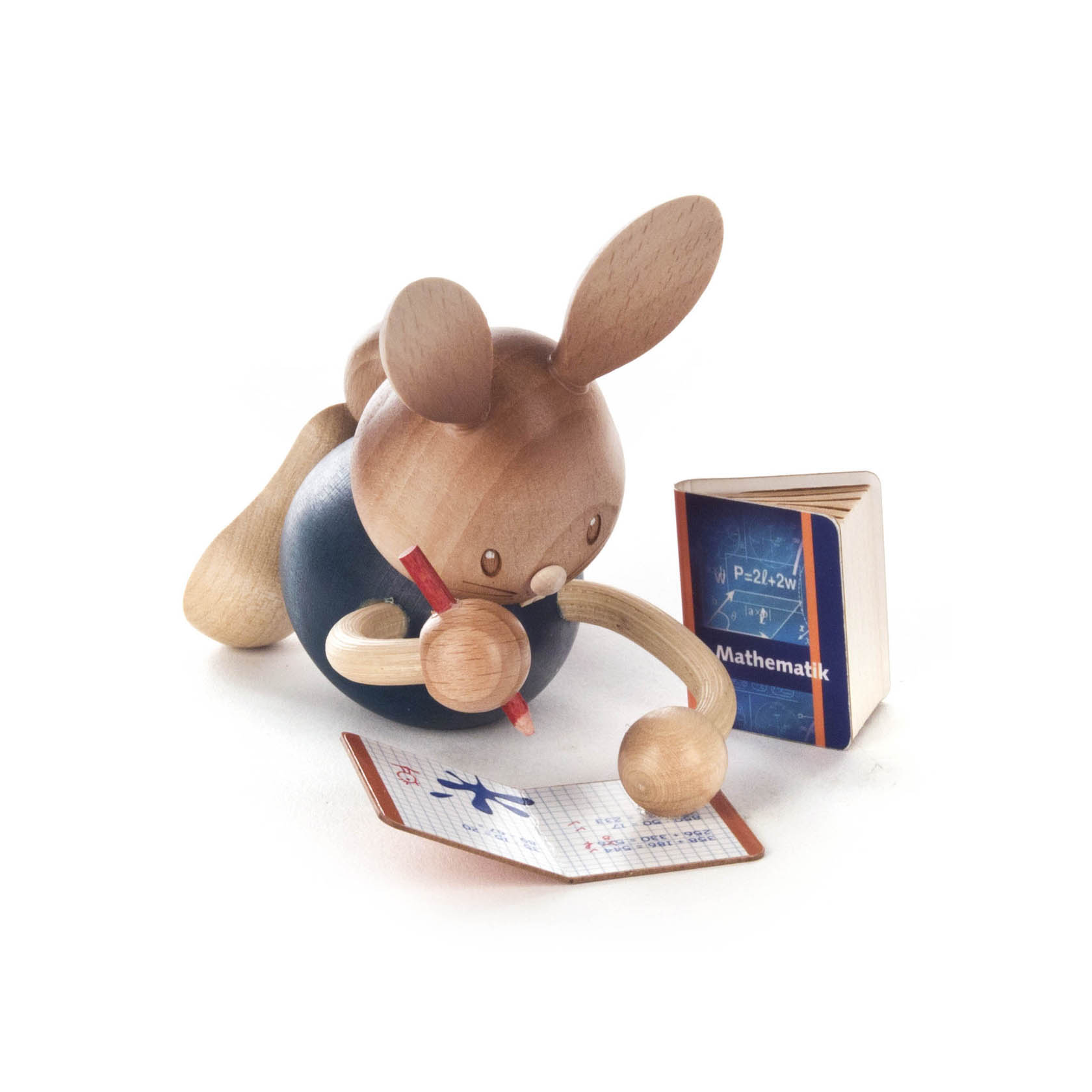 Wooden rabbit figurine named Stupsi, lying down, studying math with a pencil, open grid notebook, and a math book beside.