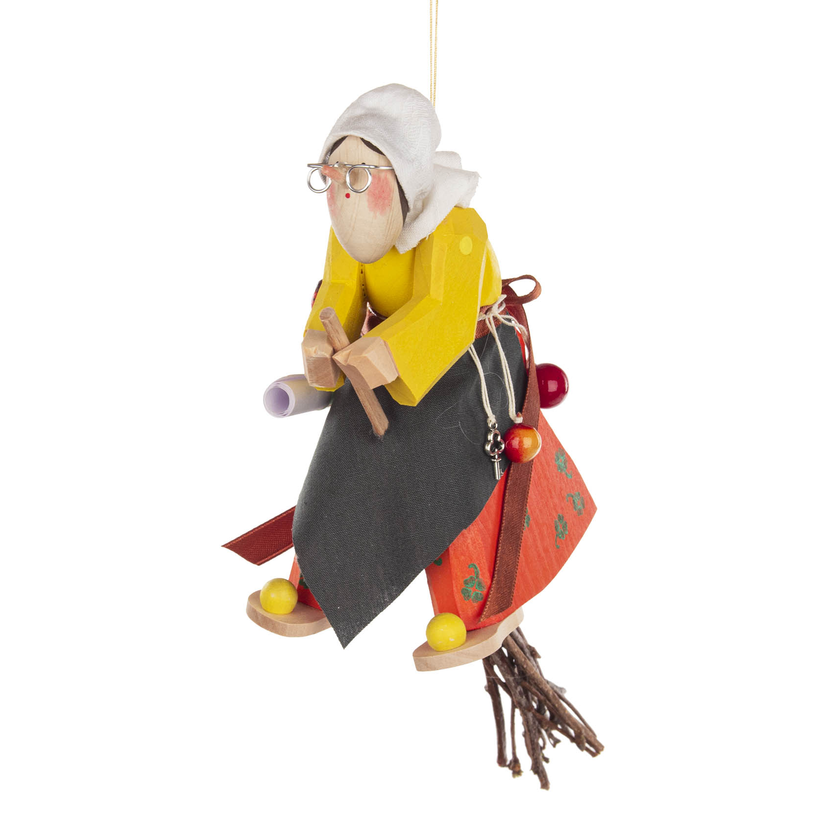 Eine handgefertigte Holzfigur einer Hexe, die auf einem Besen sitzt. Sie trägt ein gelbes Oberteil, eine schwarze Schürze, eine rote Tasche und eine weiße Haube.