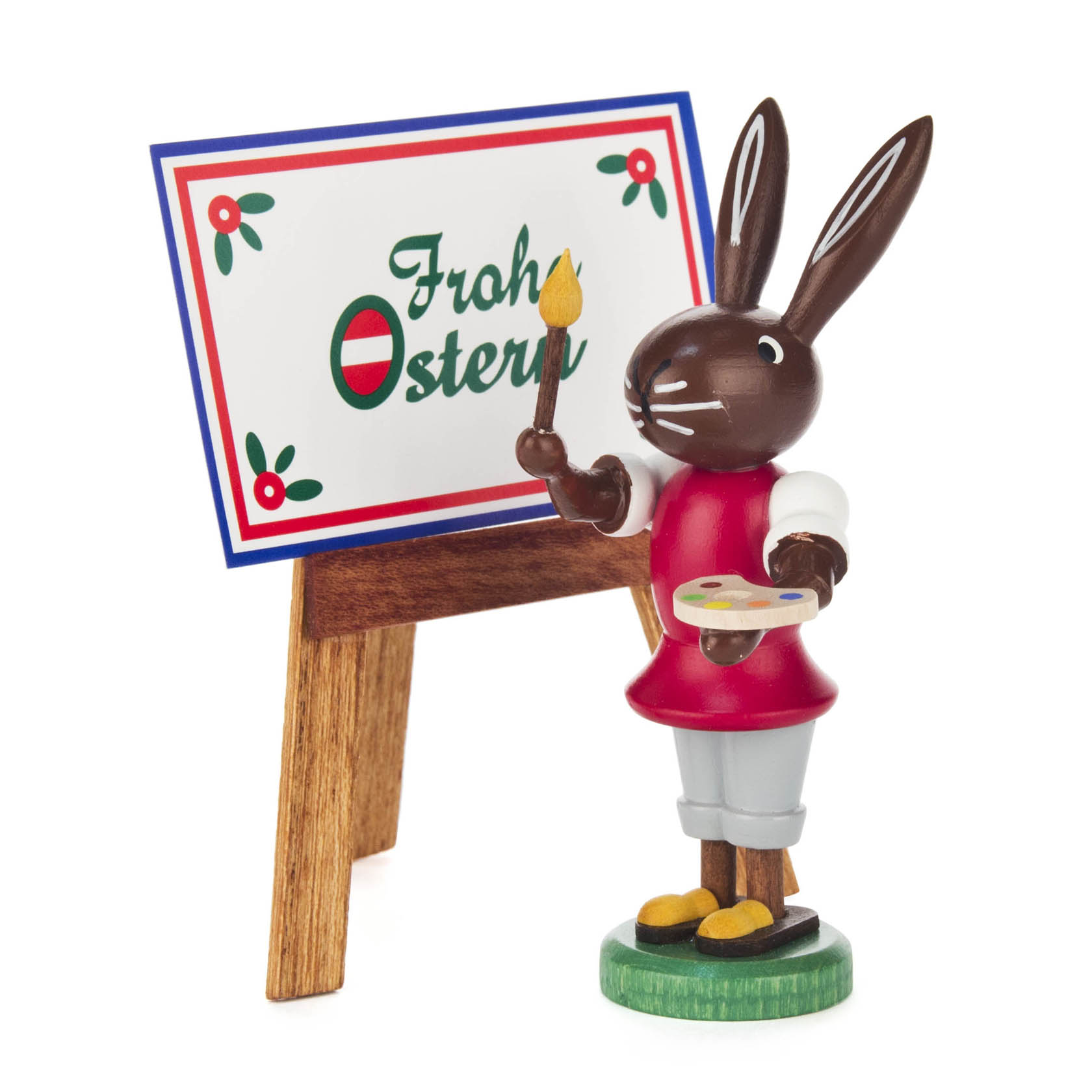 Ein dekorativer Osterhase, der eine Staffelei mit der Aufschrift 'Frohe Ostern' bemalt. Er hält einen Pinsel und eine Farbpalette in den Händen. im Dregeno Online Shop günstig kaufen