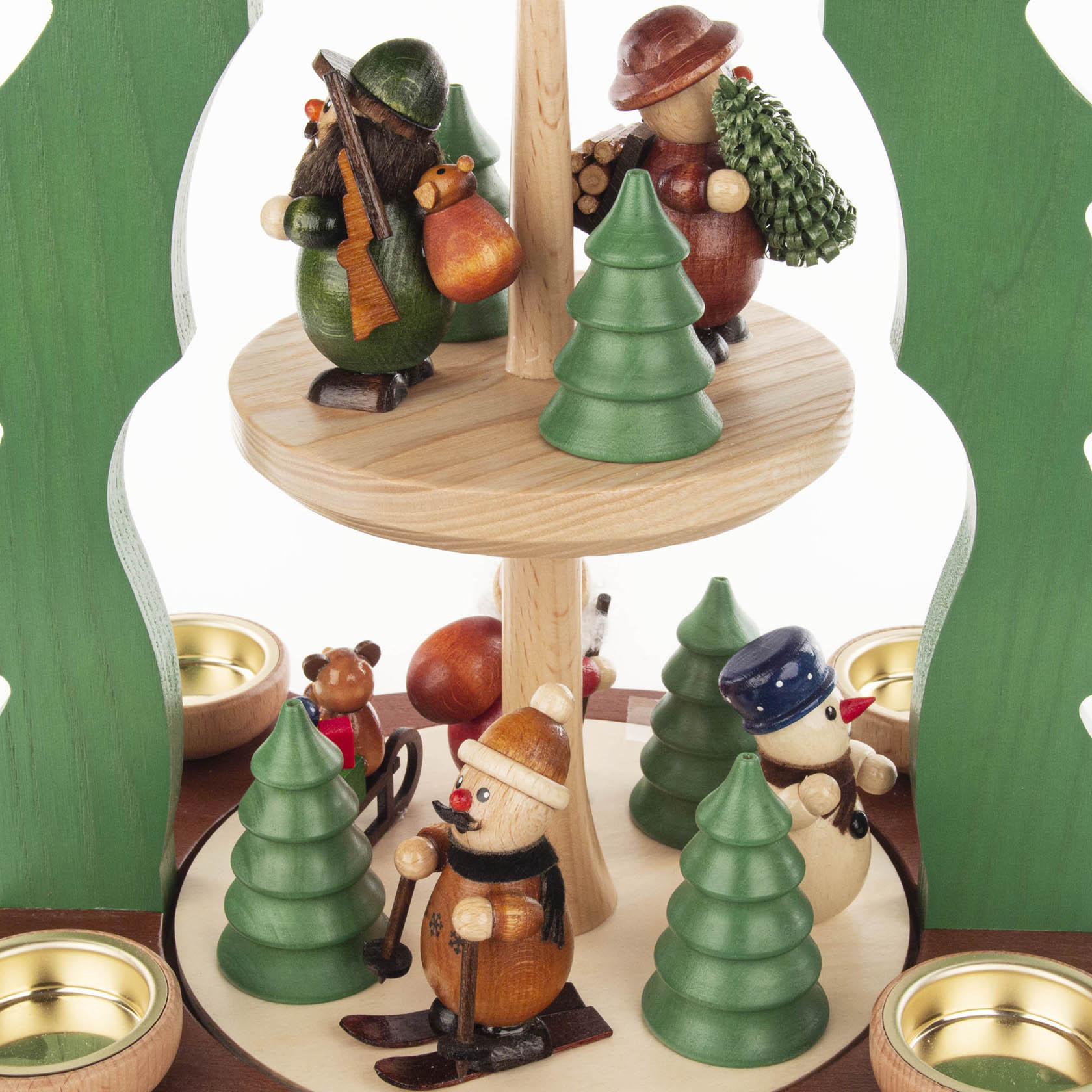Zweistöckige Weihnachtspyramide mit bunten Holzfiguren, darunter ein Skifahrer, Weihnachtsmann und Schneemann, umgeben von Teelichten und grünen Bäumen.
