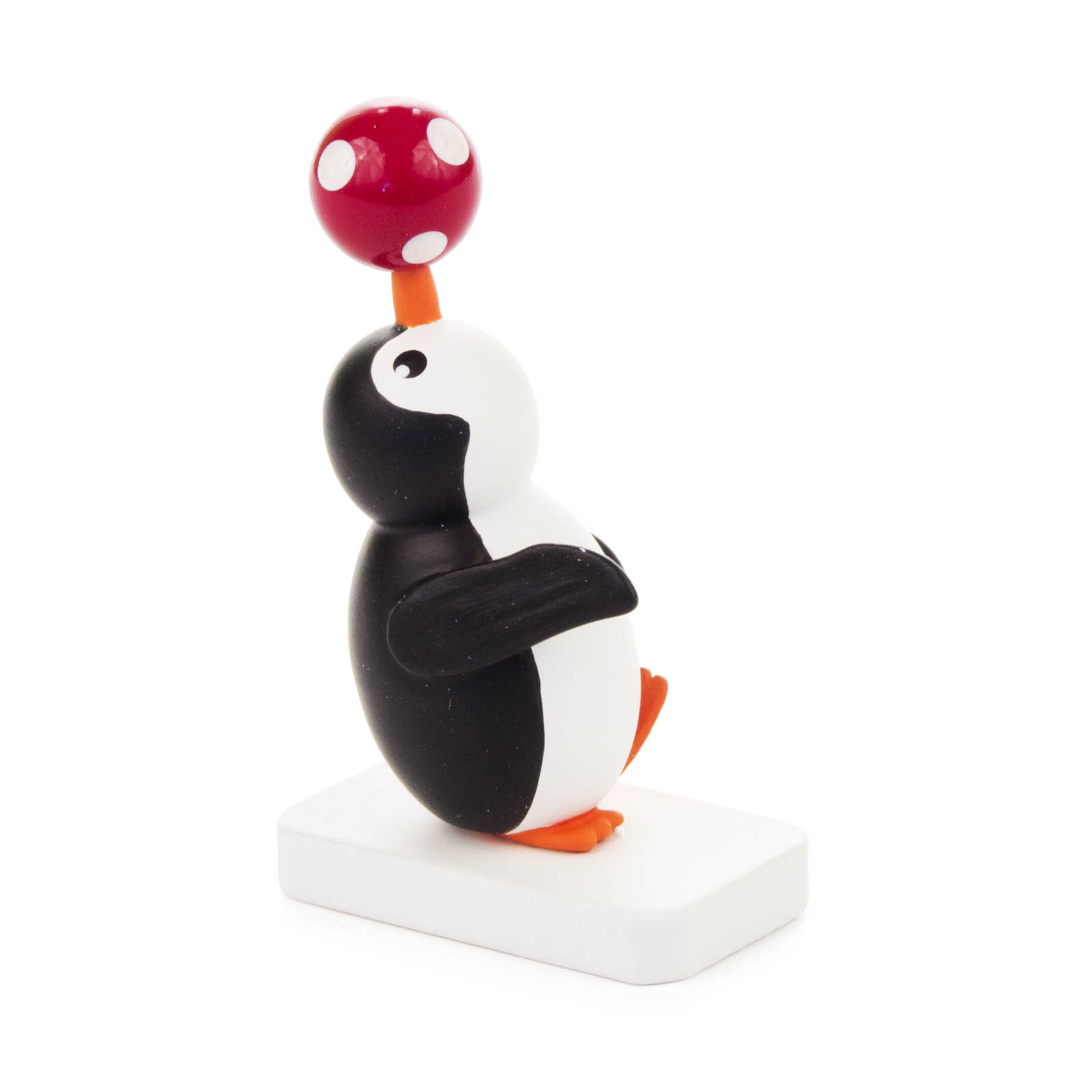 Ein plastischer Pinguin jongliert einen roten Ball mit weißen Punkten auf seinem Schnabel, stehend auf einer weißen Basis. im Dregeno Online Shop günstig kaufen