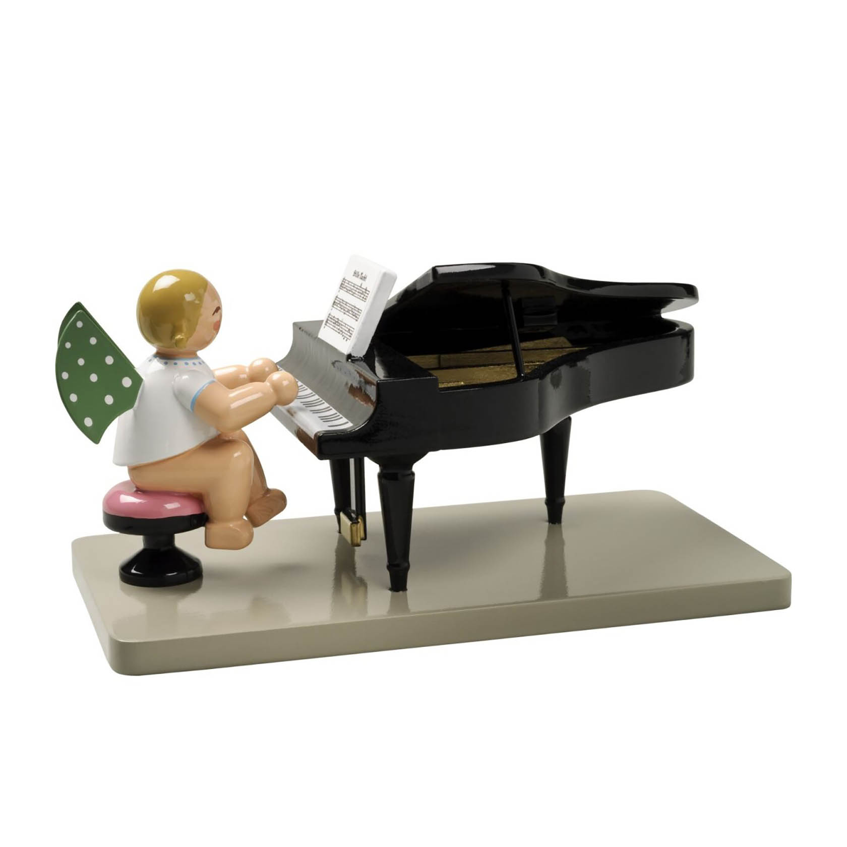 Kleine Engelsfigur mit grünen Flügeln und weißen Punkten, sitzt auf einem pinken Hocker und spielt auf einem offenen schwarzen Flügel. im Dregeno Online Shop günstig kaufen