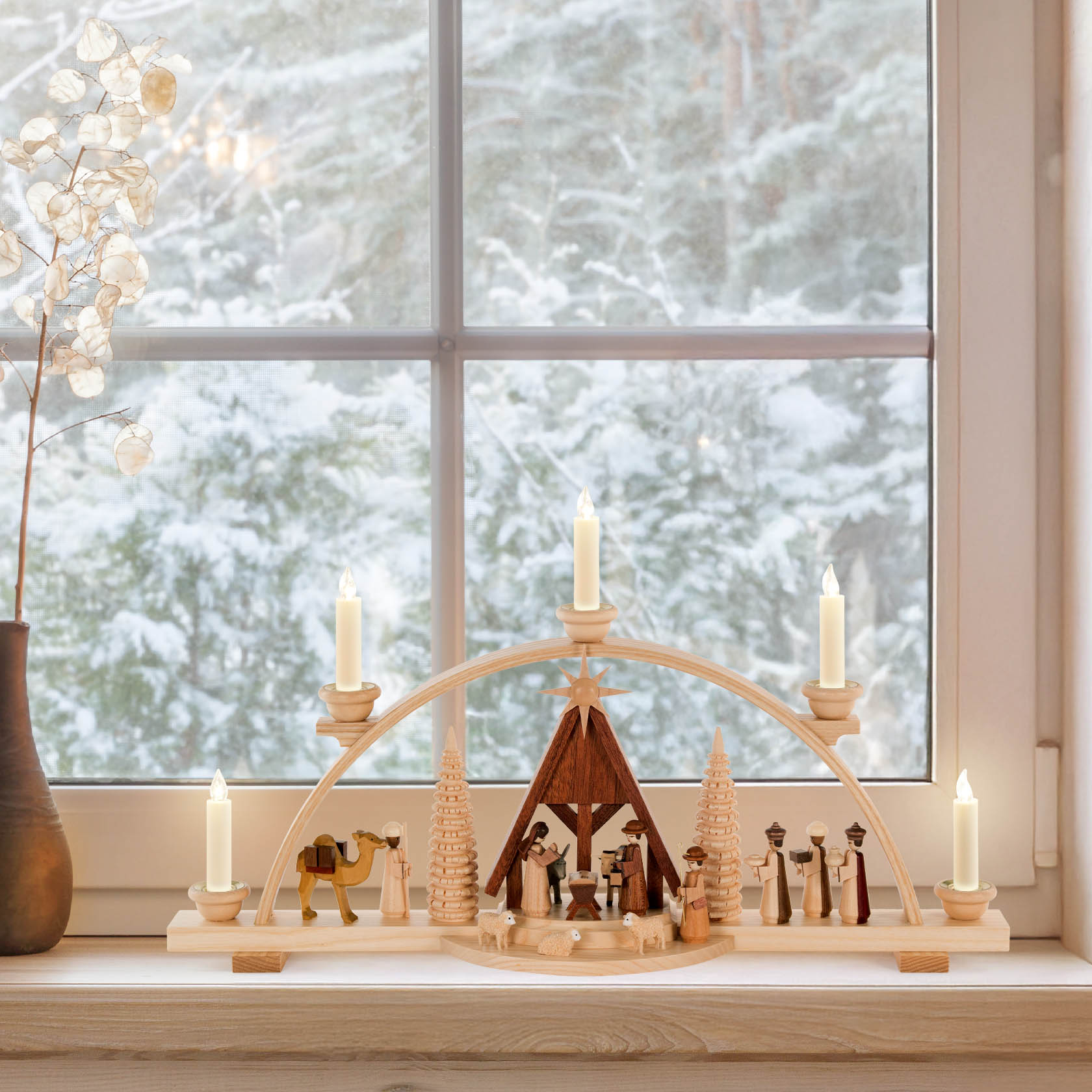 Ein Schwibbogen aus Holz zeigt die Szene der Geburt Christi mit Krippe, Maria, Josef, Jesuskind, den Heiligen Drei Königen, Tieren und Bäumen. Fünf Kerzen im Bogen.