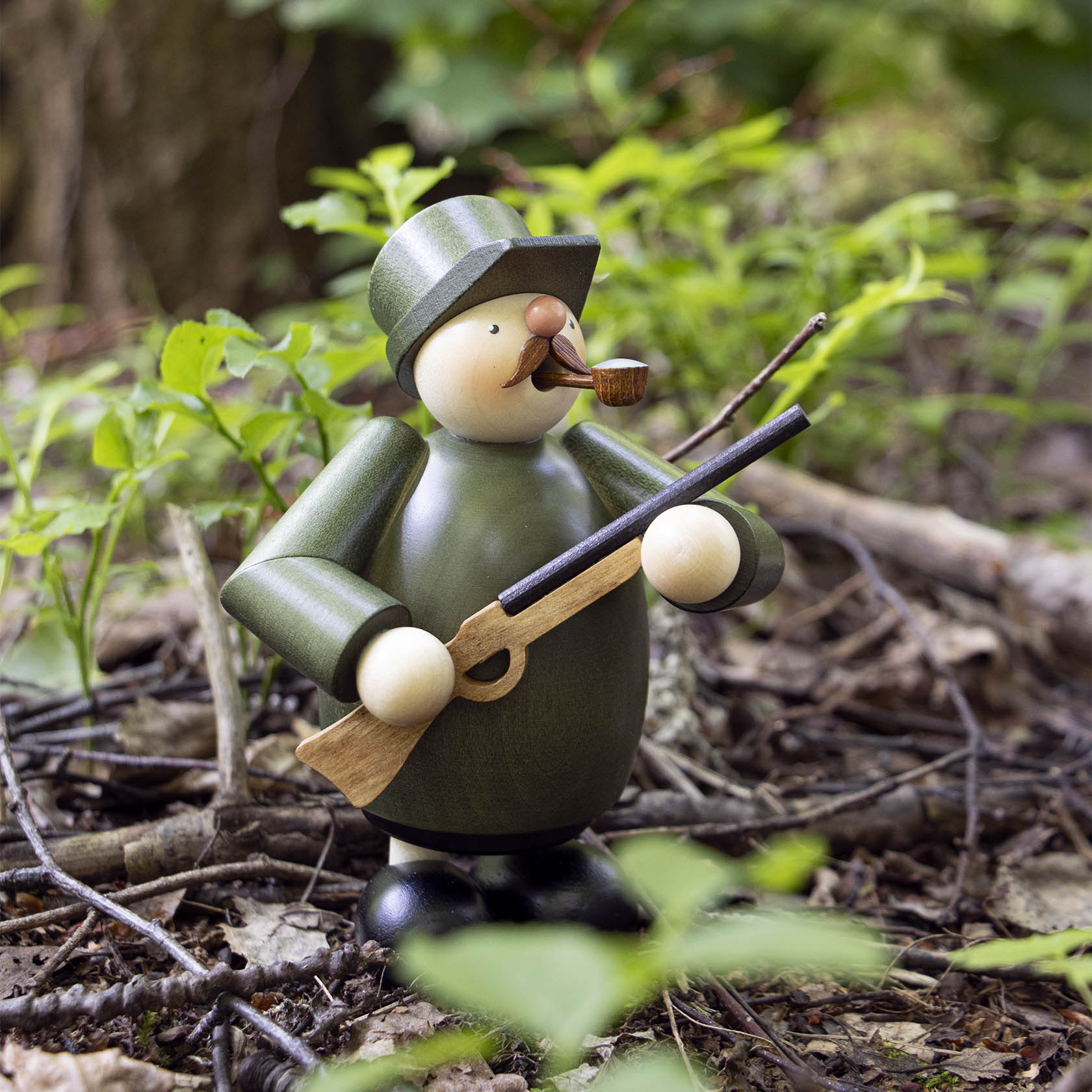 A wooden incense smoker figurine shaped like a hunter, wearing a green coat and hat, holding a rifle, with a pipe in its mouth.