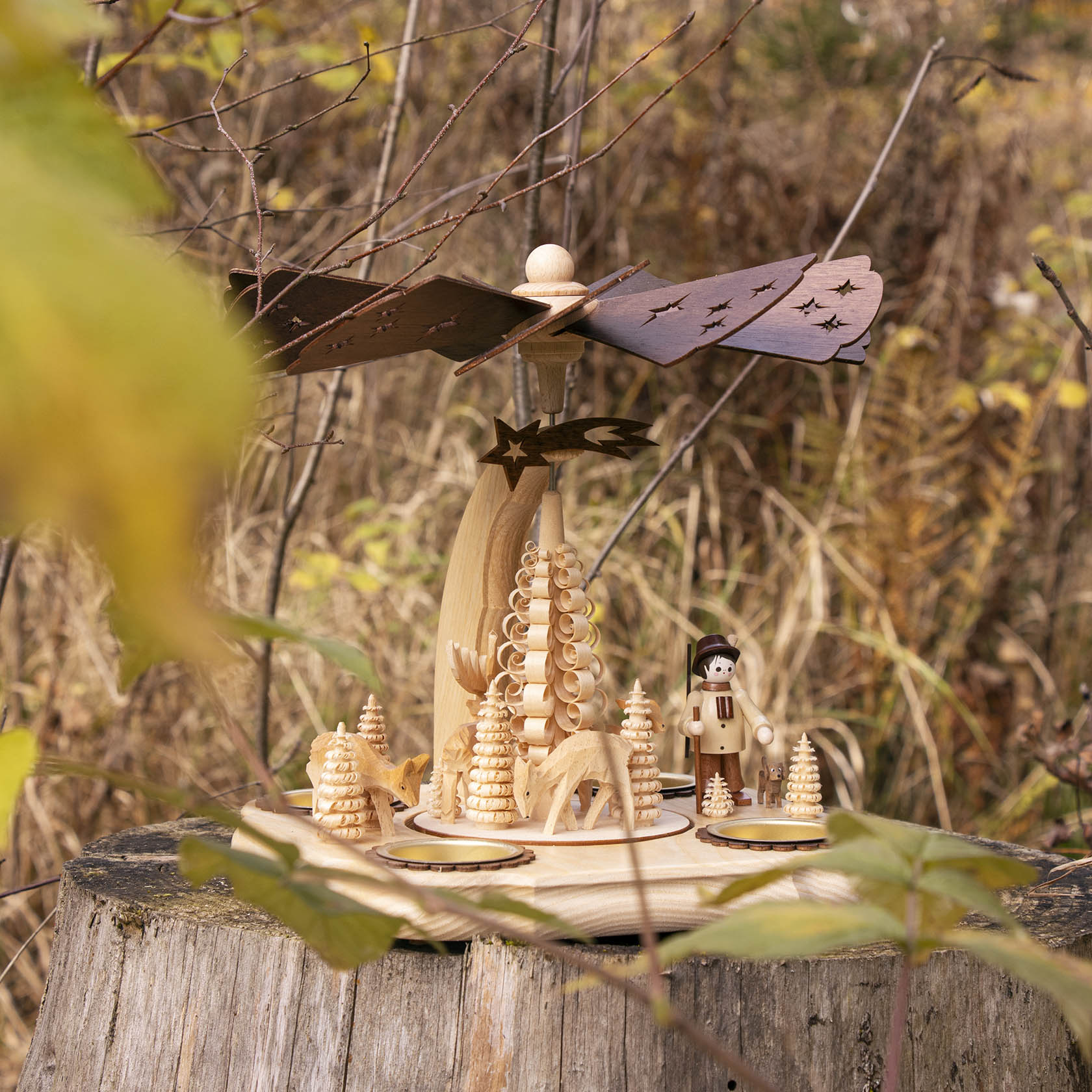 Holzpyramide auf einem Baumstumpf, mit Försterfigur, Rehen und Tannenbäumen, beweglich durch Teelichter, Detail eines Waldes im Hintergrund.