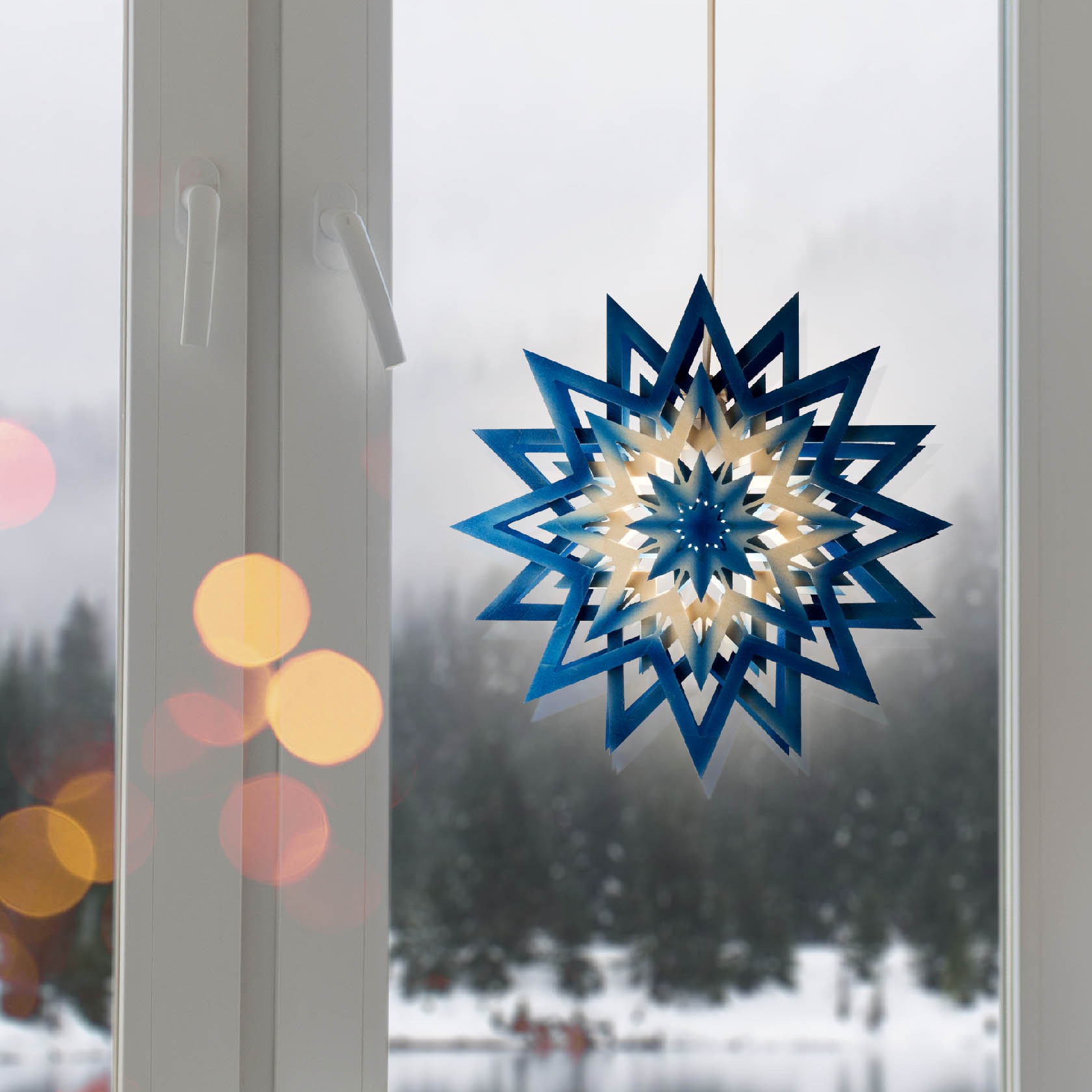 Ein blauer und natürlicher Weihnachtsstern mit elektrischer Beleuchtung hängt vor einem Fenster.