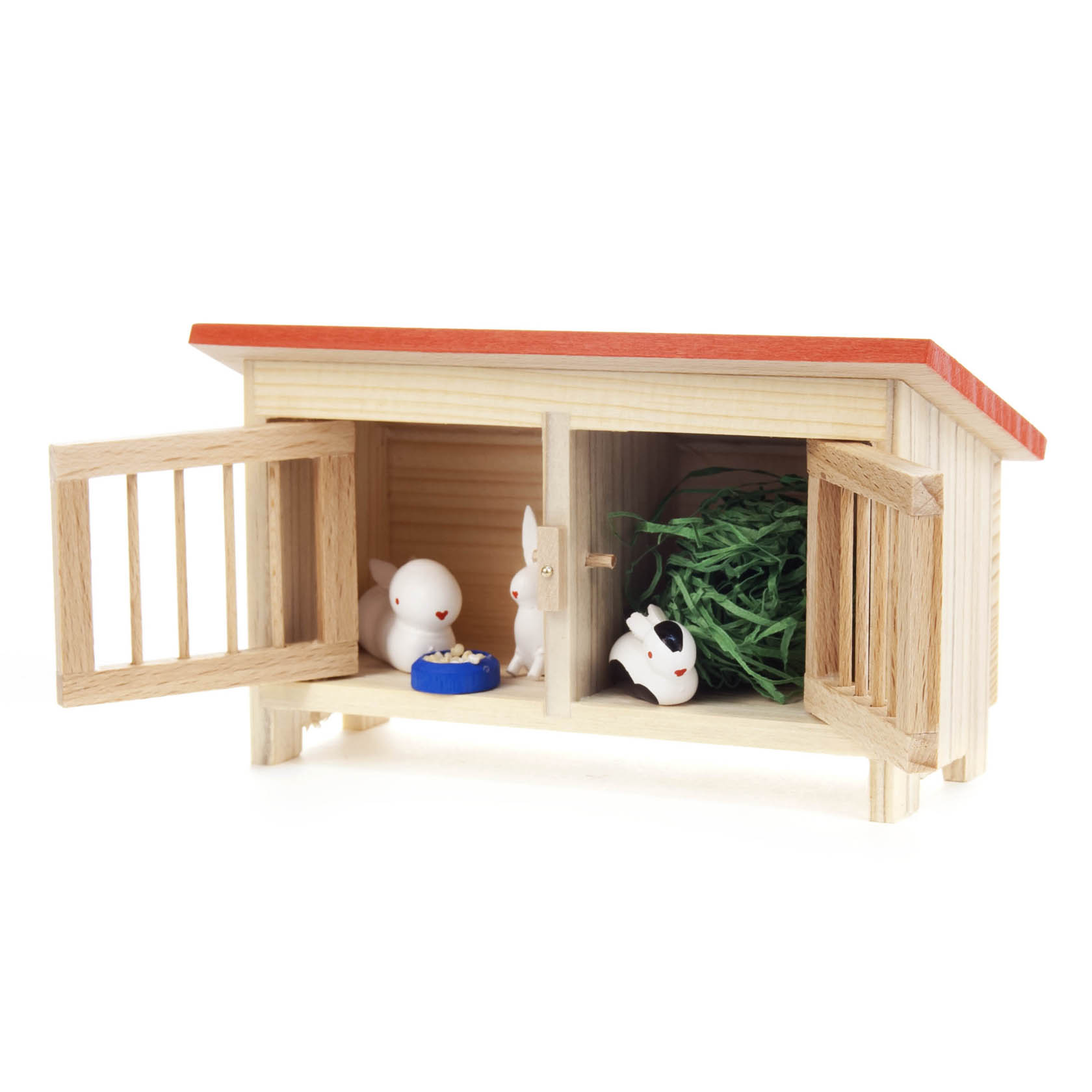 Ein kleiner Holzhasenstall mit zwei weiße Miniaturhasen, eins links mit Futter, eins rechts. Grüne Dekoration rechts im Stall. im Dregeno Online Shop günstig kaufen