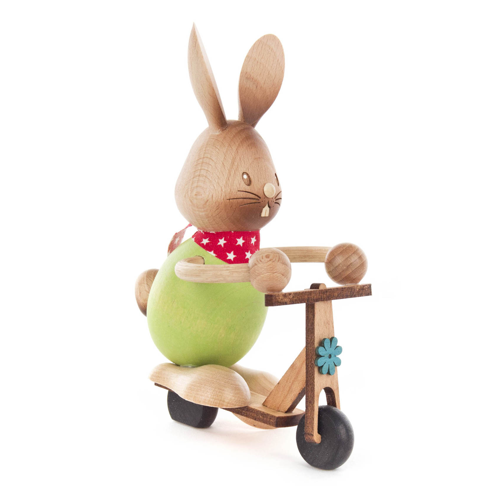 A wooden bunny figurine named Stupsi, wearing a red scarf with white stars, riding a wooden scooter with a green body and blue flower decoration.