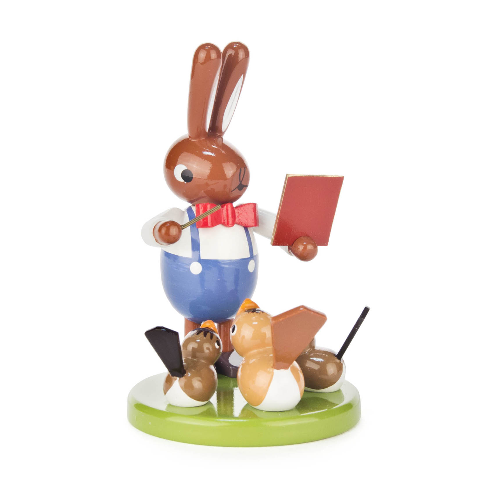 Holzfigur eines Hasen im blauen Overall und roter Fliege, der ein Buch hält, umgeben von zwei singenden Vögeln auf grünem Sockel. im Dregeno Online Shop günstig kaufen