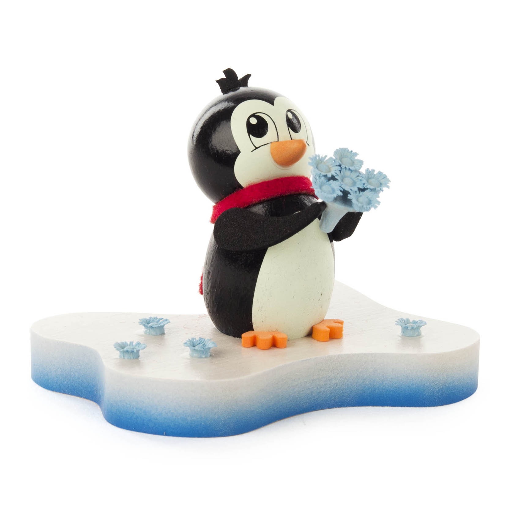Niedliche Pinguin-Figur mit rotem Schal hält einen kleinen Strauß blauer Blumen und steht auf einer weißen Plattform mit blauen Blumen darauf. im Dregeno Online Shop günstig kaufen