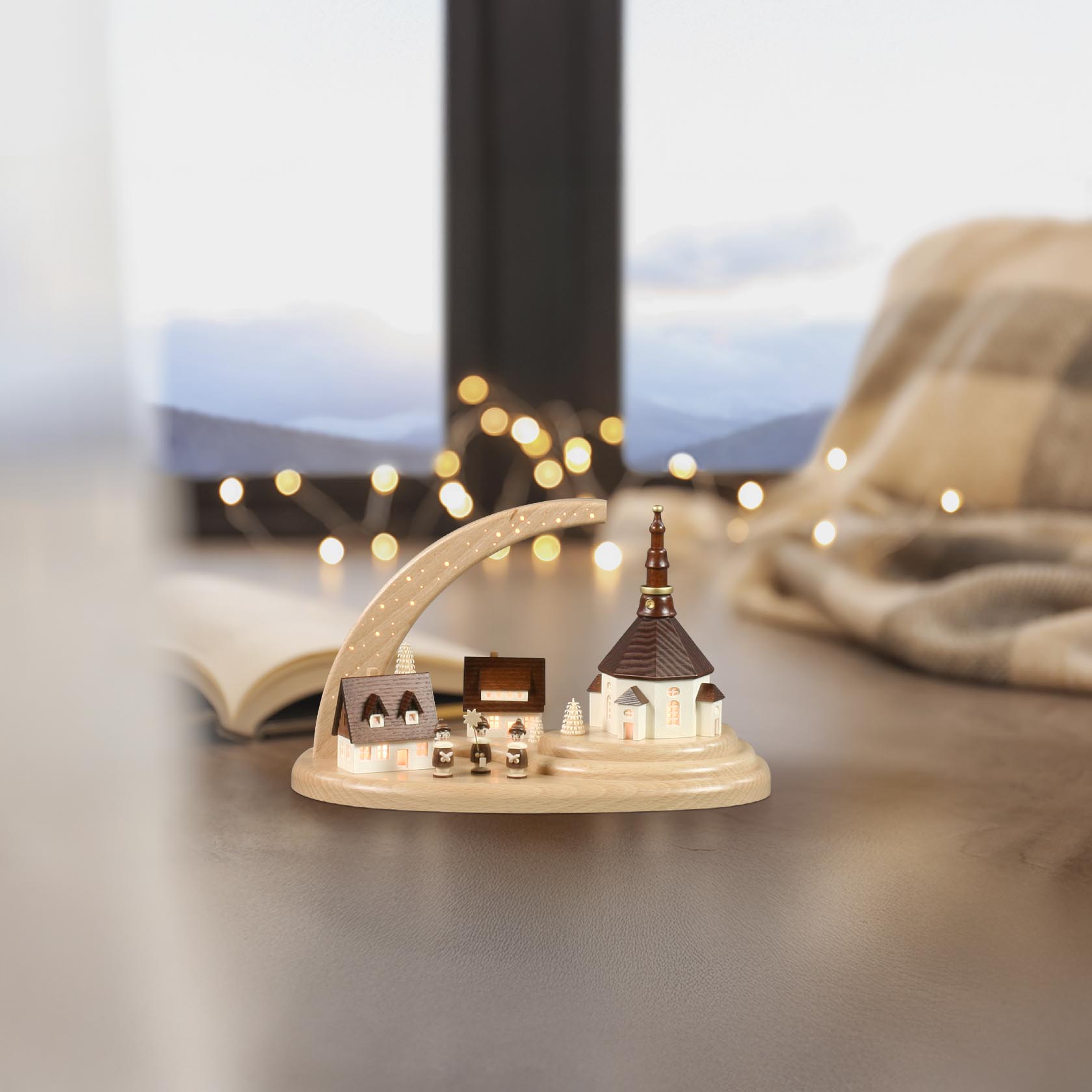 Dekorative Szenerie aus Miniaturhäusern und einer Kirche, alle beleuchtet auf einem Holzsockel mit sternenverziertem Bogen.
