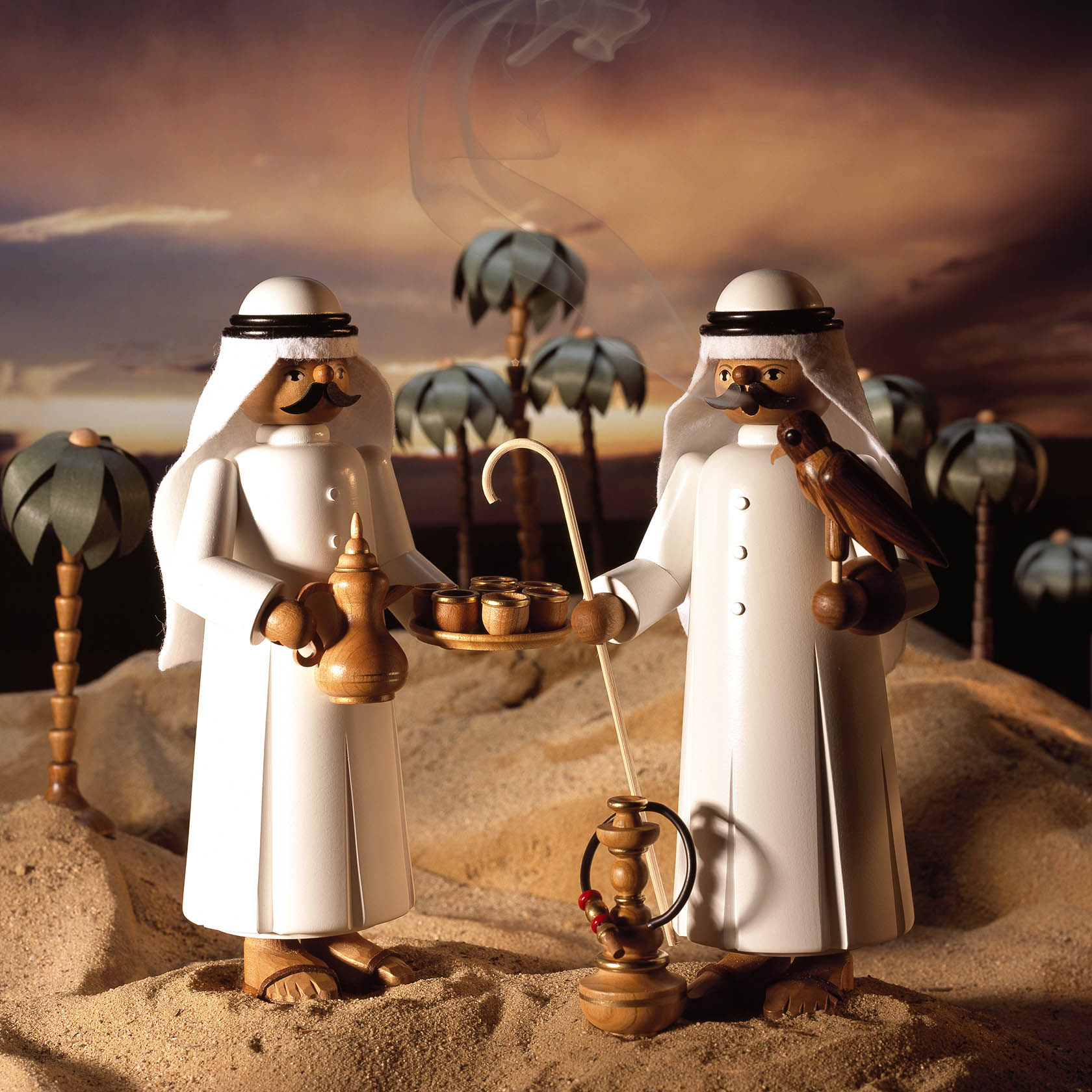Two wooden figurines dressed in traditional Arabic clothing, one holding a falcon and the other a shisha, set against a desert backdrop.