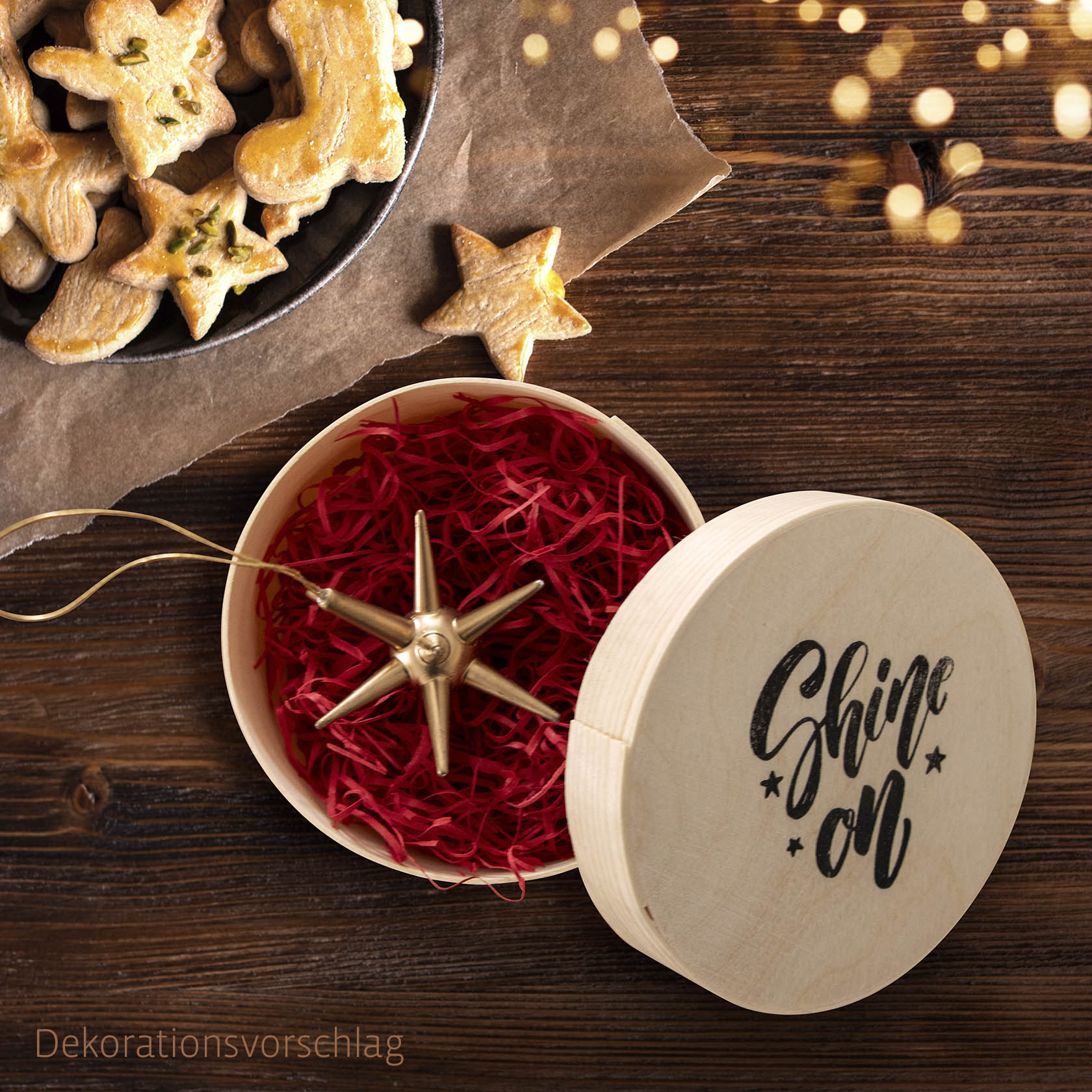 Ein goldfarbener Stern zum Aufhängen liegt in einer offenen runden Spandose mit rotem Füllmaterial. Der Deckel zeigt den Schriftzug 'Shine on'. im Dregeno Online Shop günstig kaufen