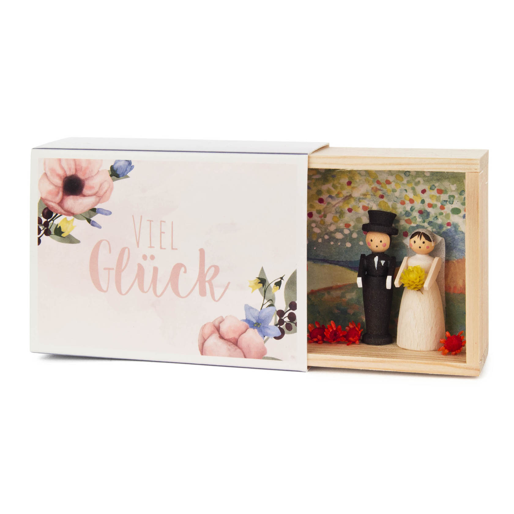 Holzbox mit einem Brautpaar aus Holzfiguren, der Bräutigam im schwarzen Smoking und die Braut im weißen Kleid, umgeben von roten Blumen. Die Box zeigt den Text 'Viel Glück'.
