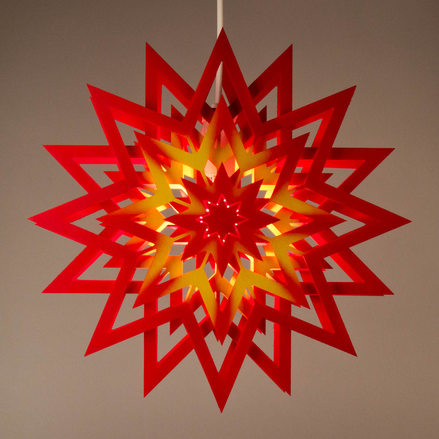 Leuchtender roter Weihnachtsstern mit gelbem Mustern und elektrischer Beleuchtung, aufgehängt in einem Raum.
