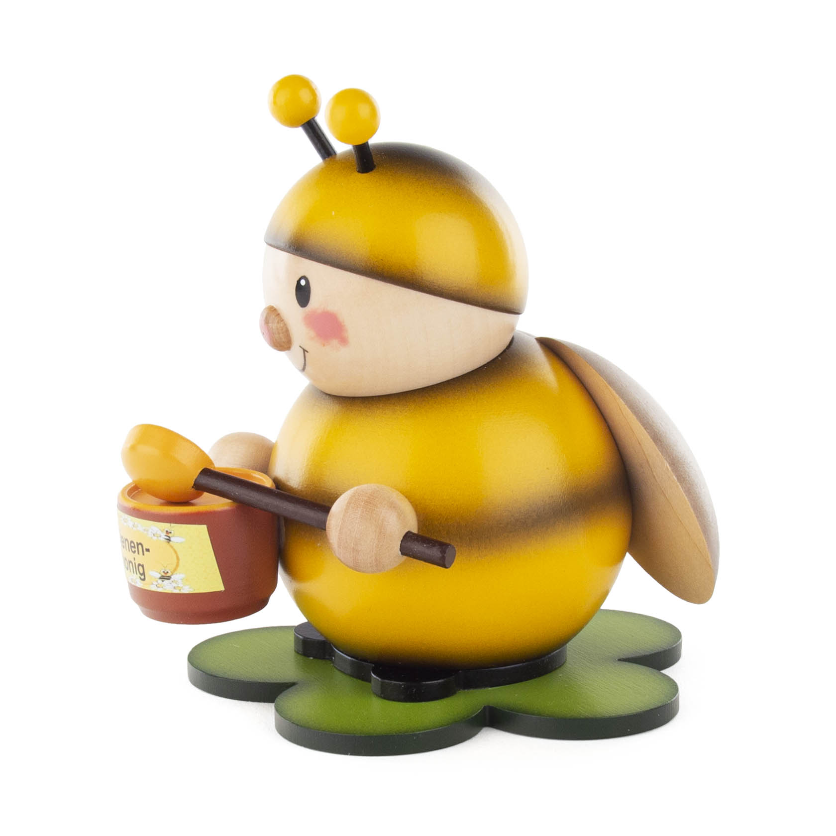 Holzfigur einer lächelnden Hummel mit gepunkteten Wangen, die einen Honigtopf mit einem Löffel in ihren Händen hält. Die Hummel steht auf einem grünen, blattförmigen Sockel.