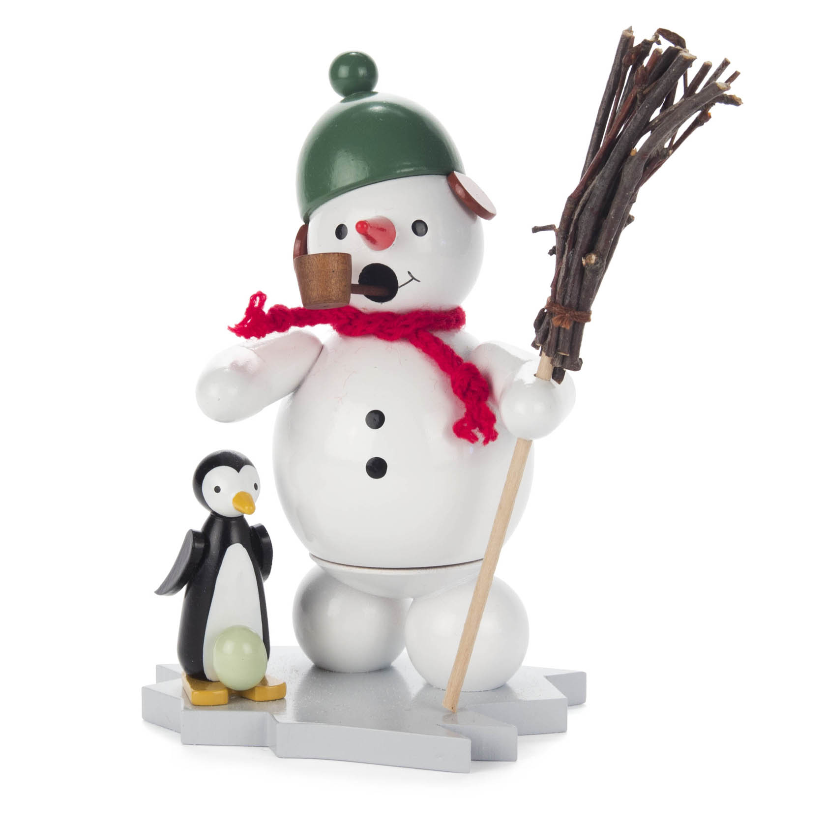 Holzfigur eines Schneemanns mit grünem Helm, Pfeife, rotem Schal, einem Besen und einem schwarzen Pinguin mit grünem Ei auf einer weißen Fläche. im Dregeno Online Shop günstig kaufen