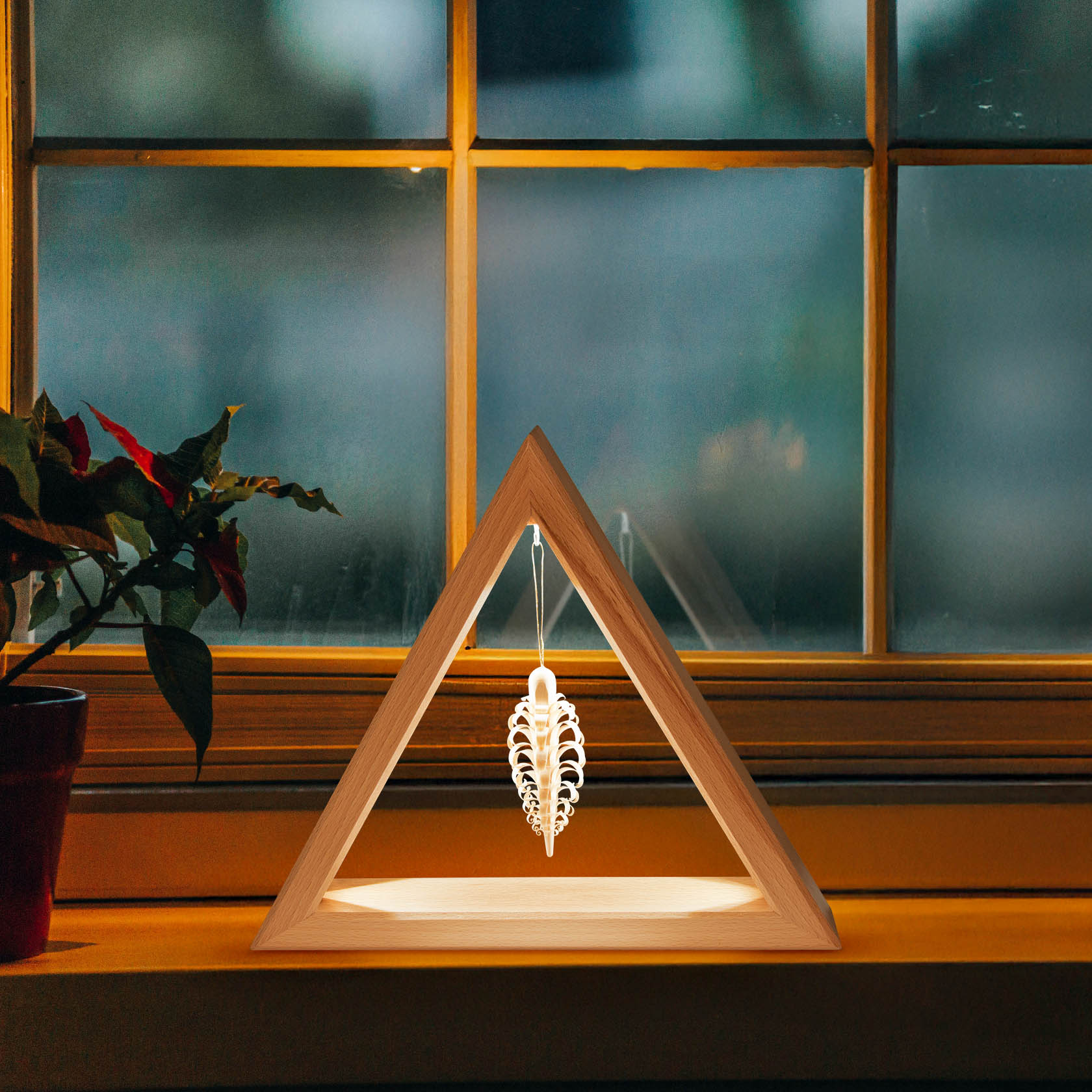 Ein dreieckiger Holzrahmen mit einem innen hängenden, beleuchteten Ornament steht vor einem Fenster. Das Ornament wird von einem LED-Band beleuchtet.