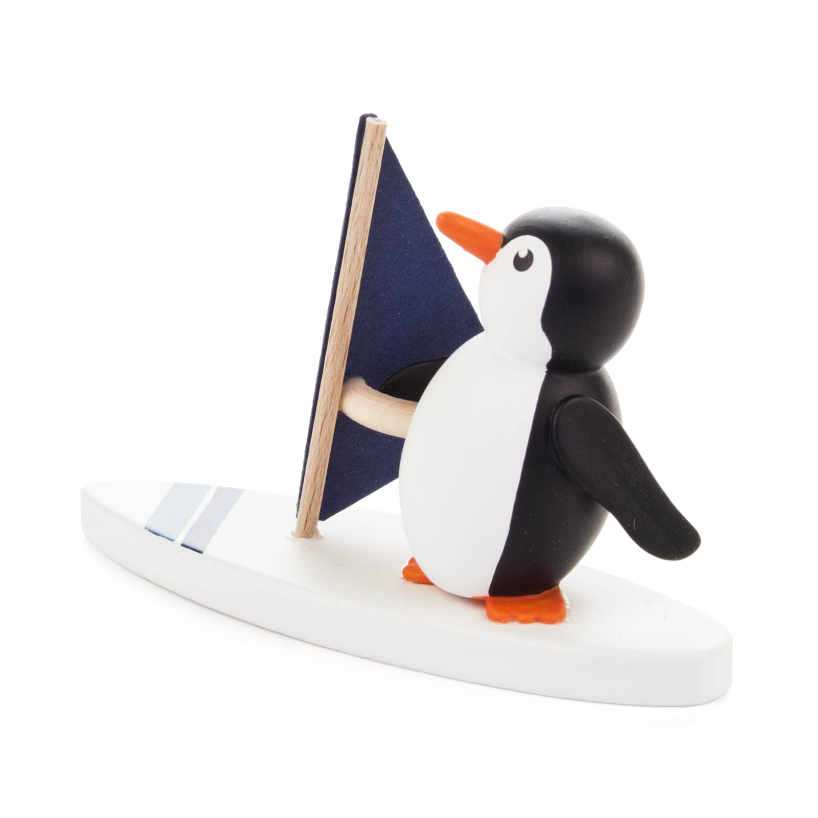 Kleine Pinguinfigur aus Holz, die auf einem weißen Surfbrett mit blauem Segel steht. Der Pinguin ist schwarz-weiß mit orangem Schnabel und Füßen. im Dregeno Online Shop günstig kaufen