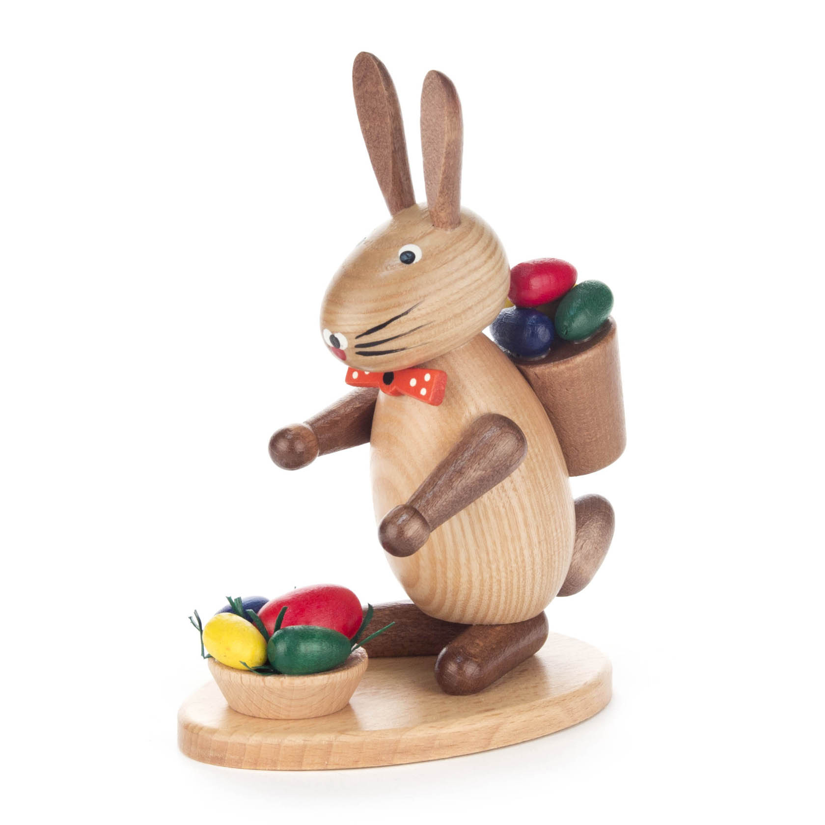 Holzhase mit roter Fliege trägt einen Korb mit bunten Eiern auf dem Rücken und steht neben einer Schale mit weiteren bunten Eiern. im Dregeno Online Shop günstig kaufen