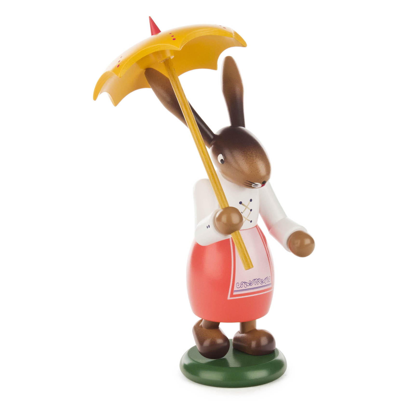 Eine farbenfrohe Osterhäsin-Figur steht aufrecht und hält einen gelben Schirm. Sie trägt eine traditionelle Schürze in Rot und einen weißen Pullover.