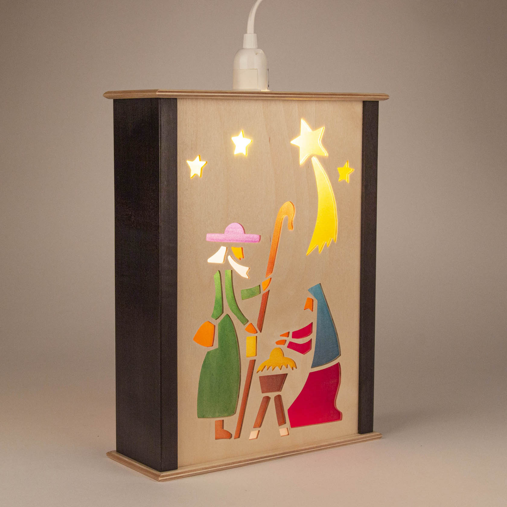 Eine beleuchtete Fensterlaterne zeigt die Geburt Christi. Zu sehen sind stilisierte Figuren von Maria, Josef und dem Jesuskind in der Krippe unter einem Sternenhimmel.