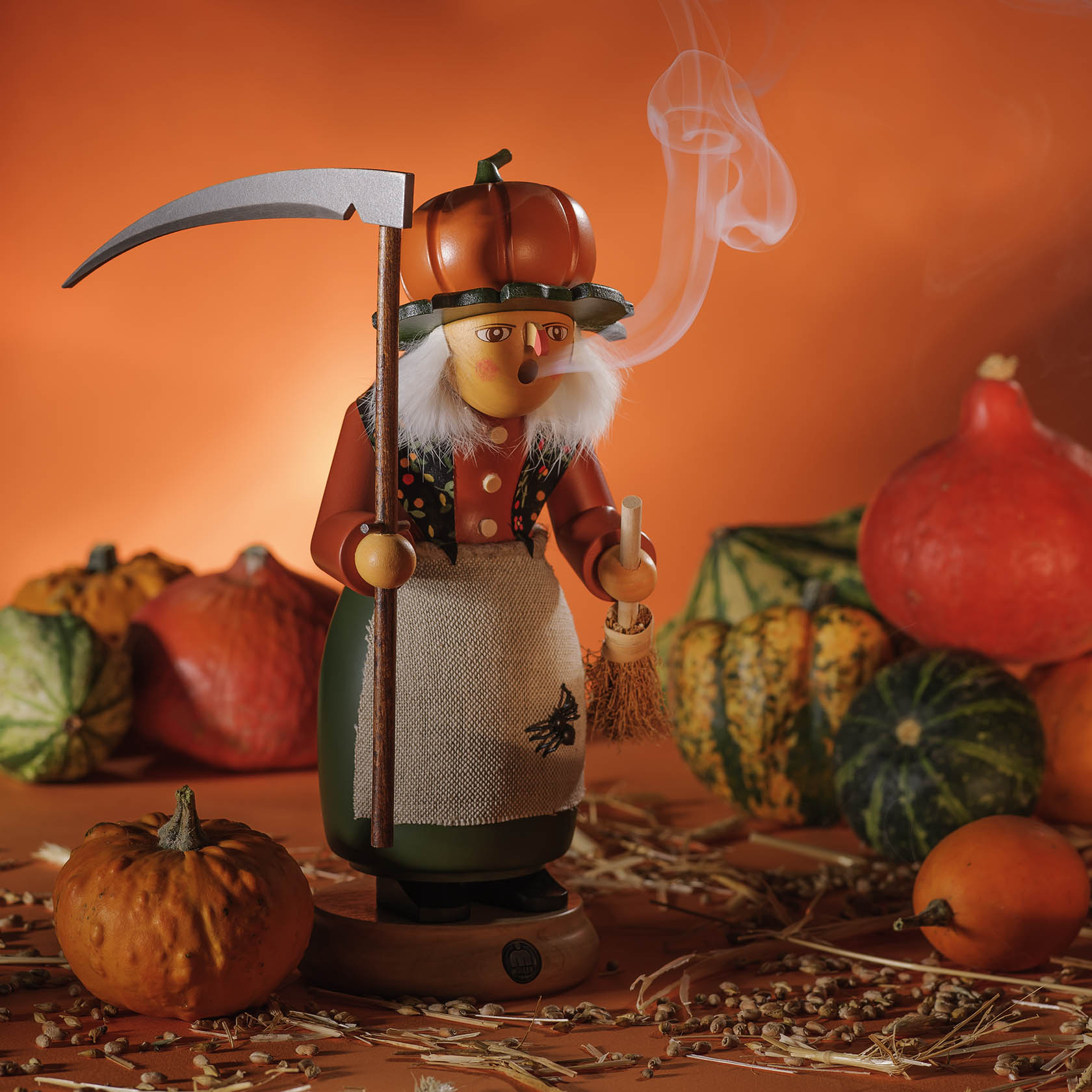 Holzfigur einer Räucherfrau in Form einer Halloween-Hexe mit weißer Haarpracht, großem Kürbis-Hut und Besen, eine Pfeife rauchend, umgeben von Kürbissen.