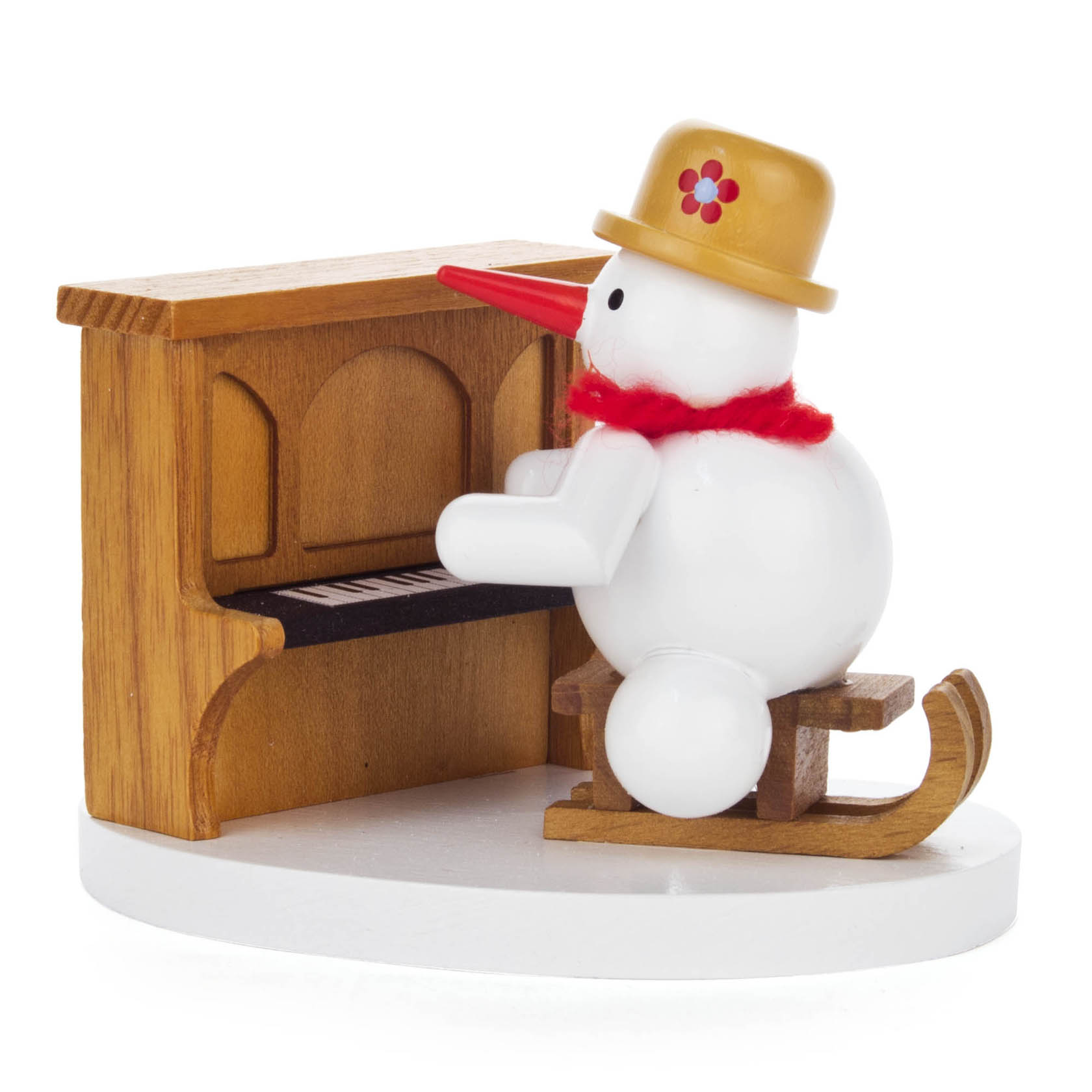 Small wooden snowman figurine playing a piano, wearing a hat and scarf, sitting on a sled.