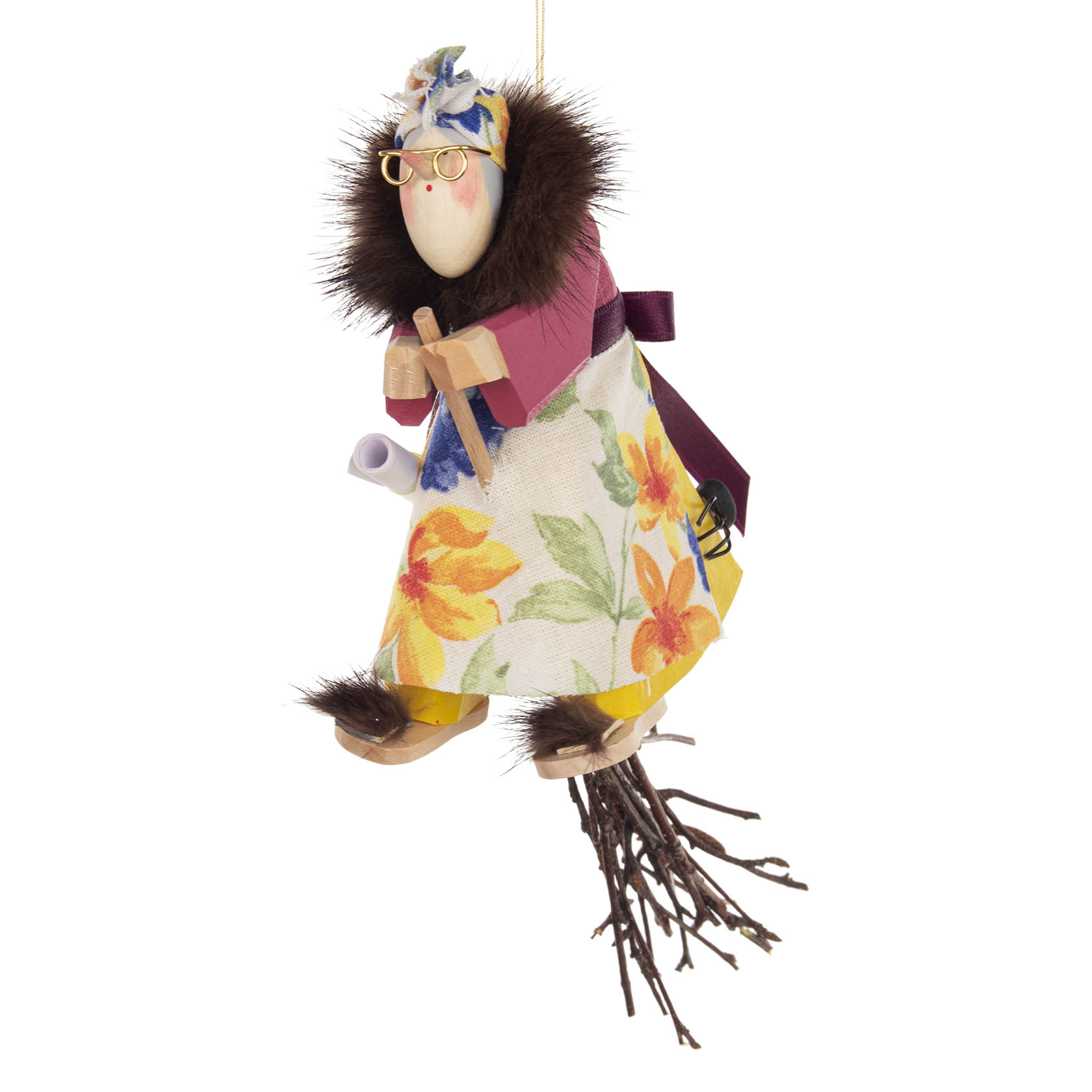 Geschnitzte Holzfigur einer Hexe mit Brille, buntem Blumenkleid, Pelzmantel, auf einem Besen reitend, mit einem Papier und einer kleinen Spinne.