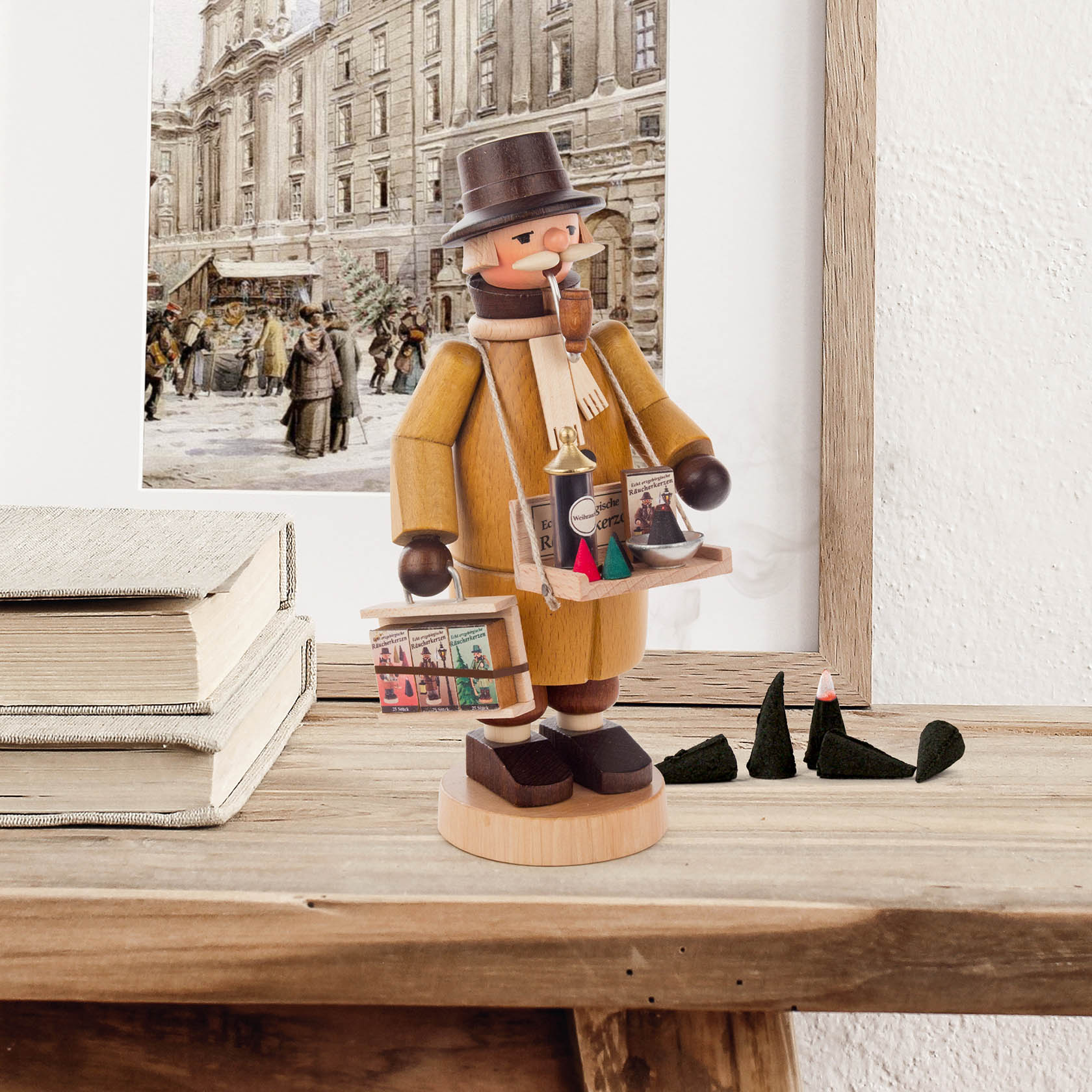 Handgefertigter Räuchermann als Räucherkerzenverkäufer mit Tablett voller Miniatur-Räucherkerzen, auf einem Tisch mit Büchern und schwarzem Kegel.