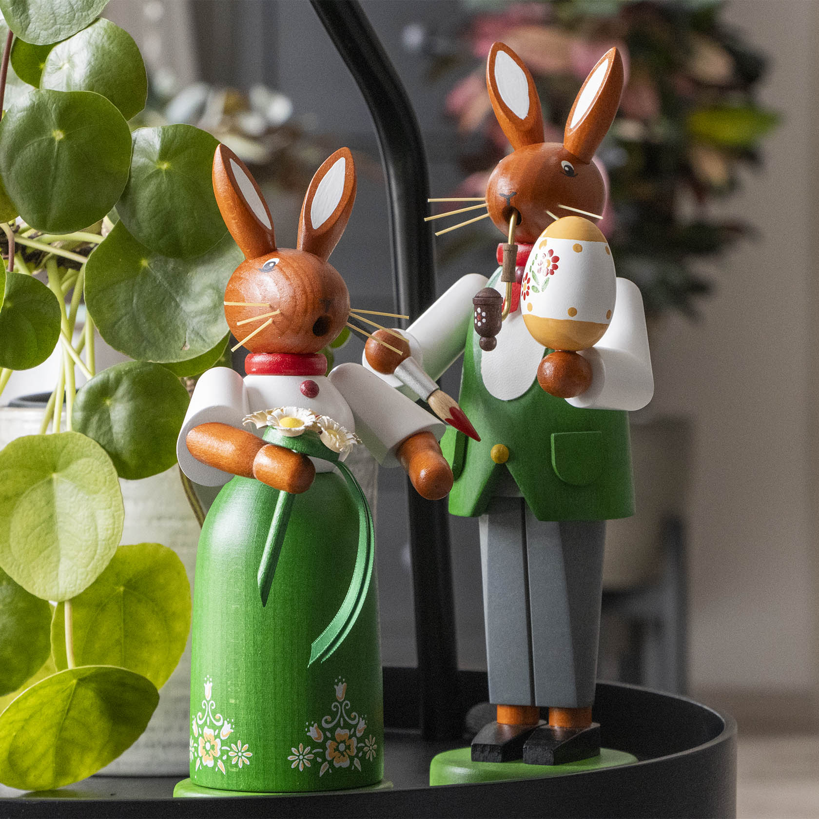 Zwei handbemalte Holzräucherfiguren in Form von Hasen. Die Hasenfrau trägt ein Kleid und hält Blumen. Der Hase trägt eine Weste und raucht aus einem Räuchergefäß.