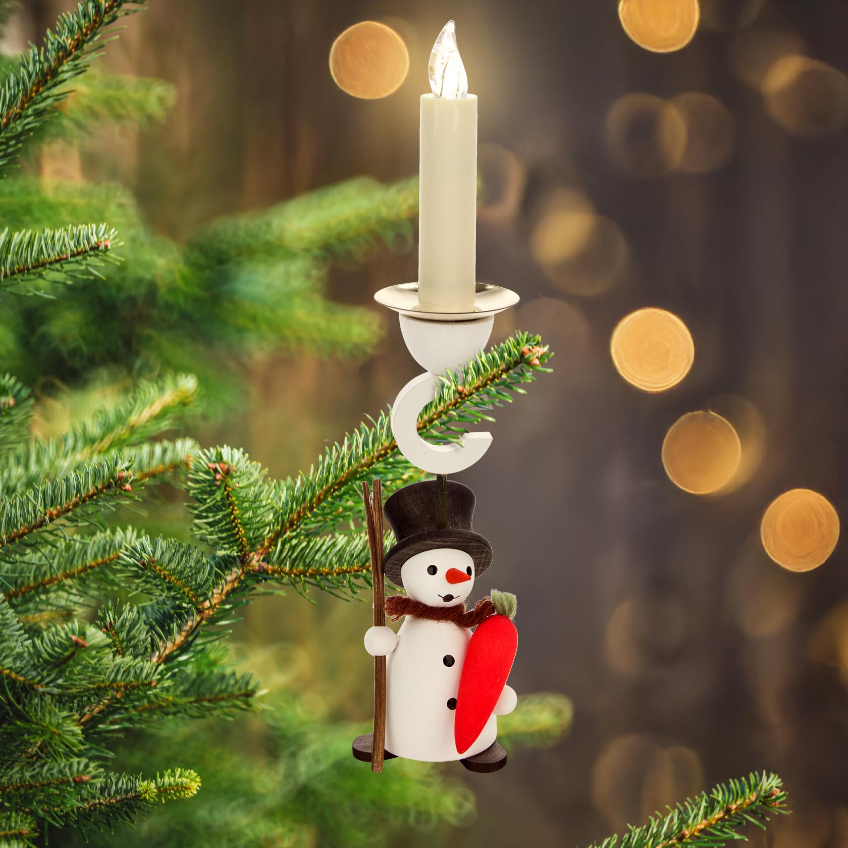 Ein Schneemann-Ornament mit Möhre und Stock hält einen Kerzenhalter mit weißer Kerze auf einem Tannenzweig.