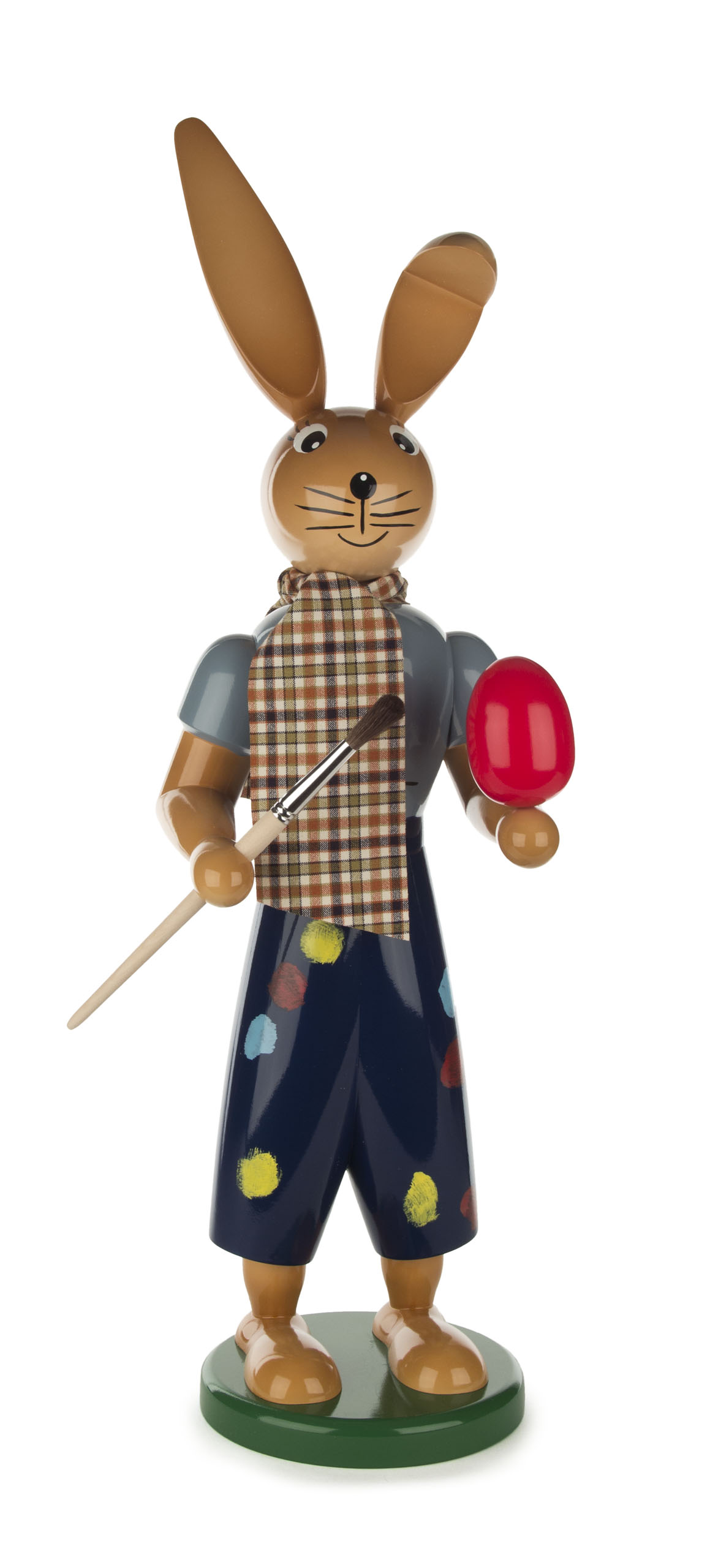Holzfigur eines Hasen mit Pinsel und rotem Osterei, trägt karierten Schal und bunte Hose.