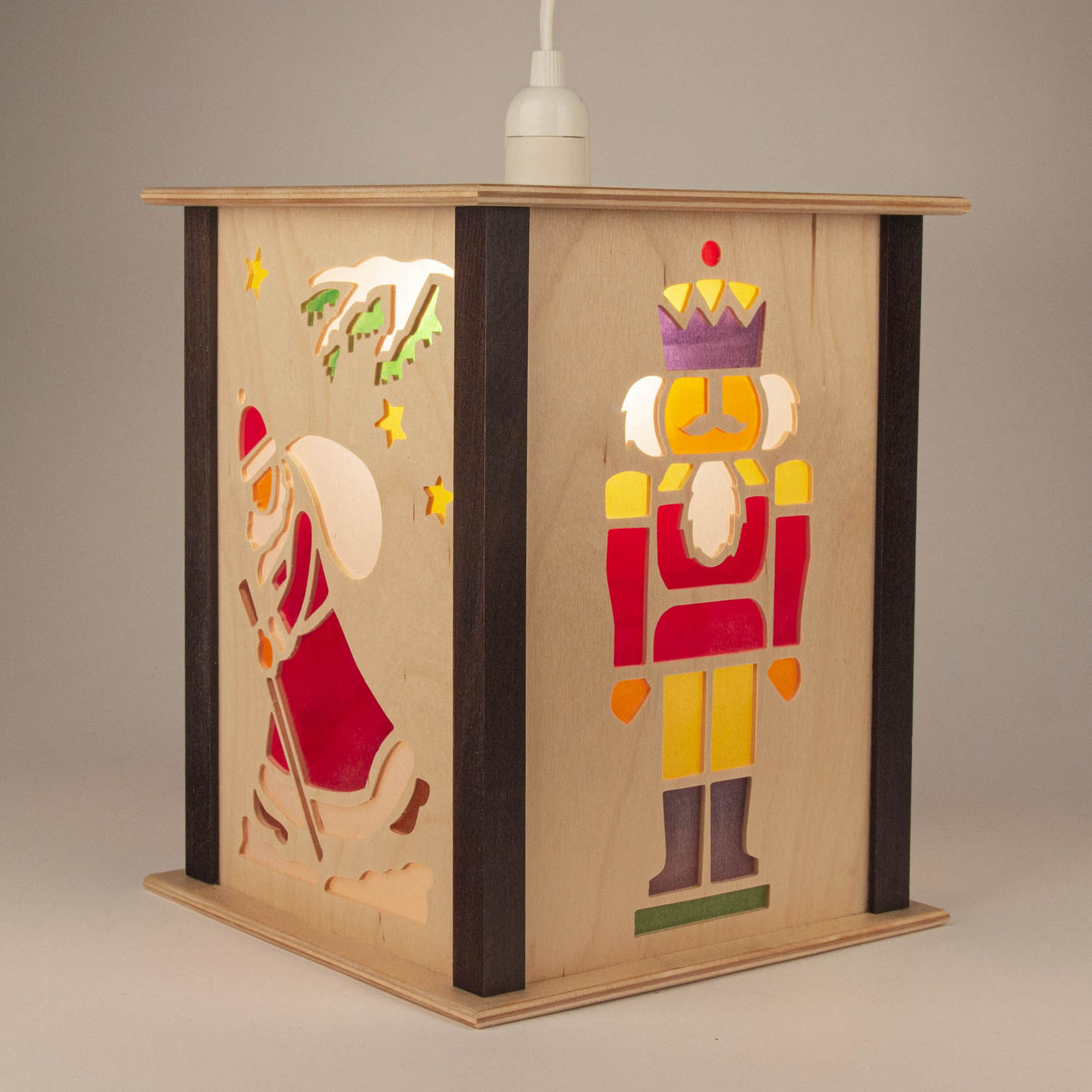 Holzlaterne mit buntem Scherenschnitt eines Nussknackers in Rot und Gelb und eines Weihnachtsmanns mit Tannenbaumzweig und Sternen.
