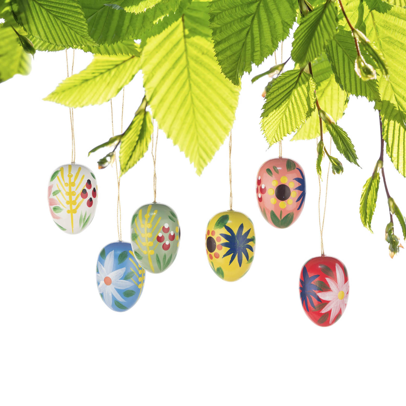 Sechs bunte Ostereier mit Blumenmuster, die an Schnüren von einem grünen Ast hängen.