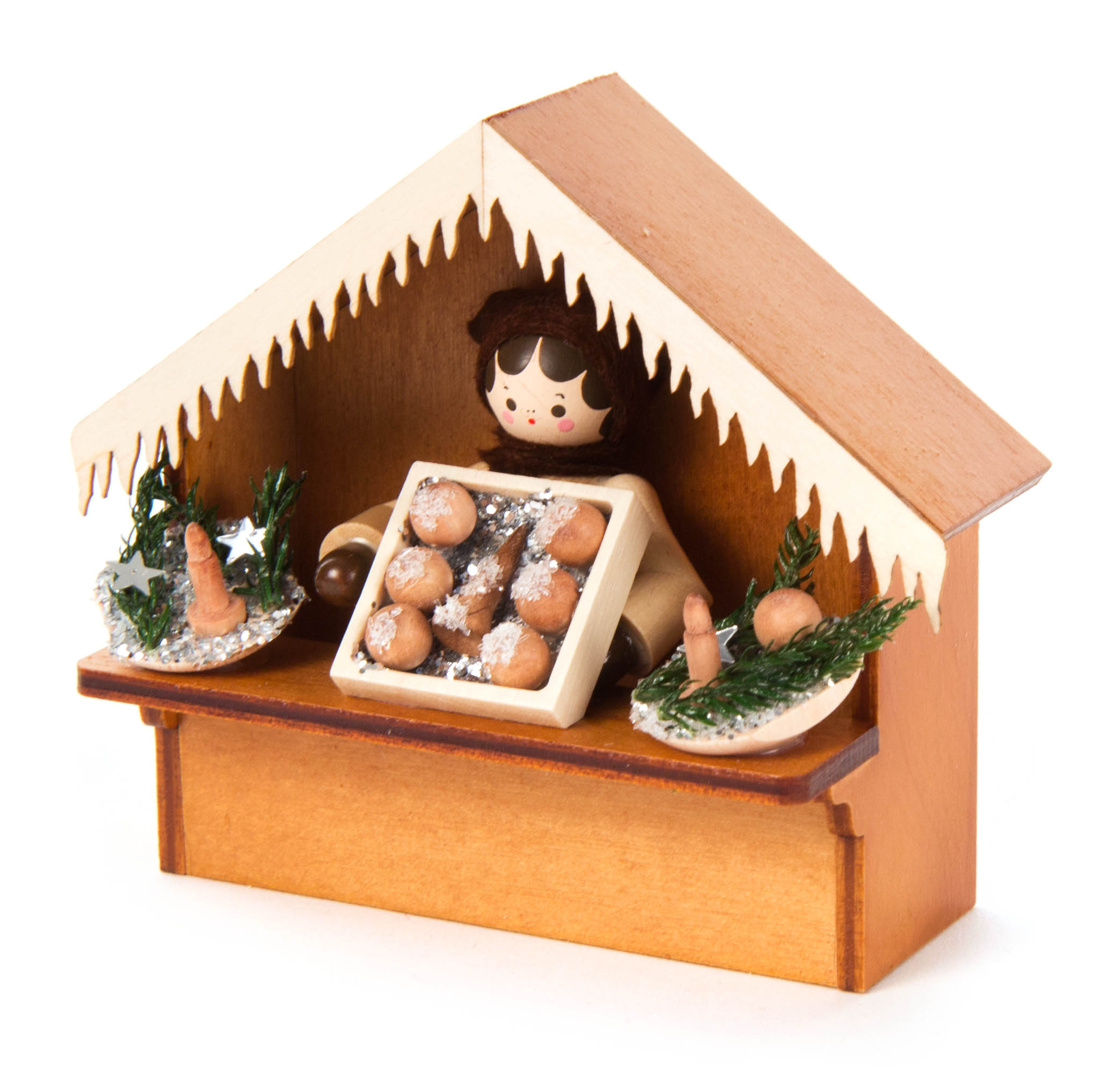 Holzfigur, die an einem Weihnachtsmarktstand aus Holz Christbaumschmuck verkauft. Der Stand ist mit einem spitzen Dach und zwei Dekorationen versehen.