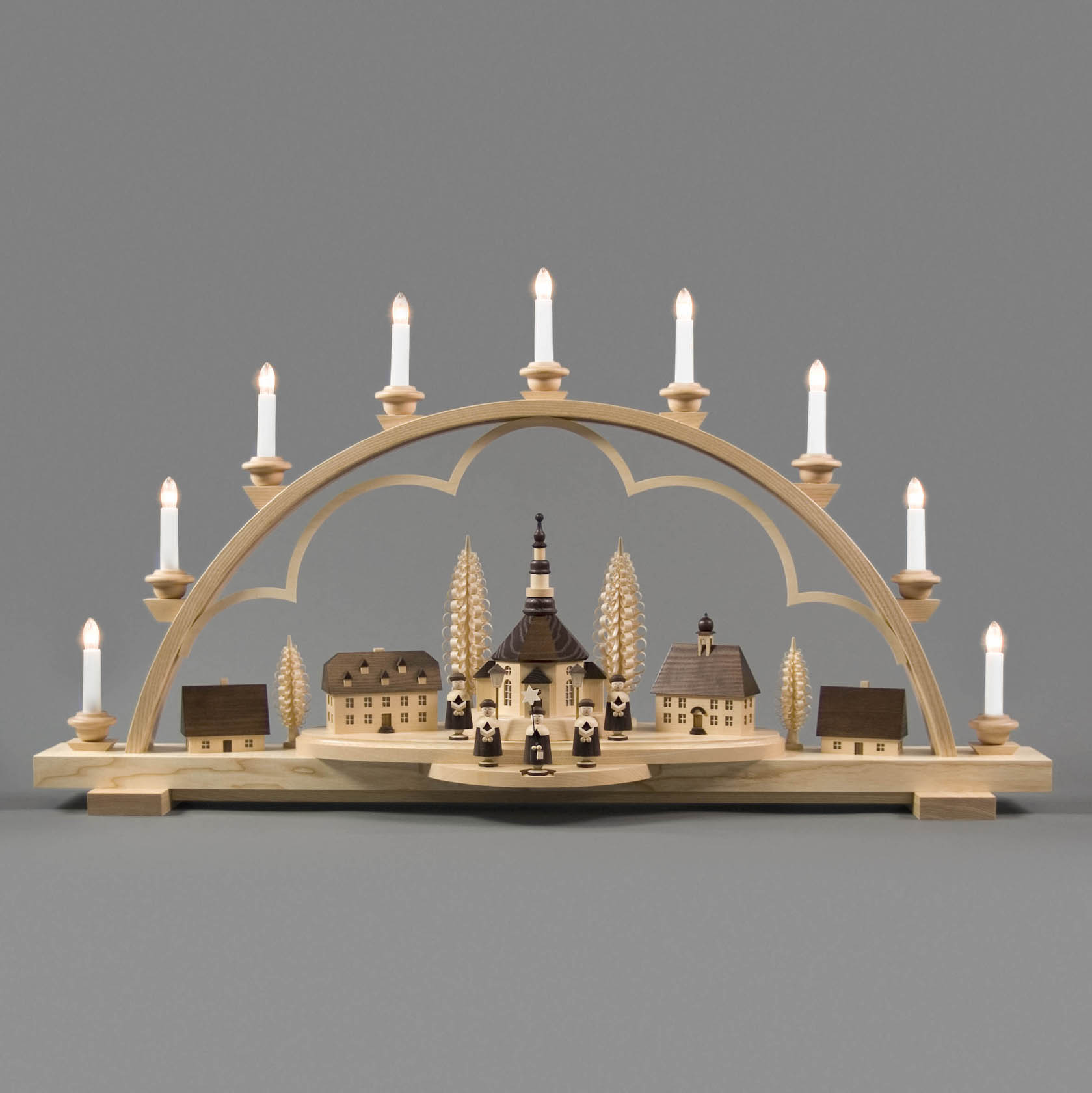 Ein Schwibbogen aus Holz mit einem Seiffener Dorf und Kurrende Figuren, elektrisch beleuchtet mit innenbeleuchteten Gebäuden und Laternen.